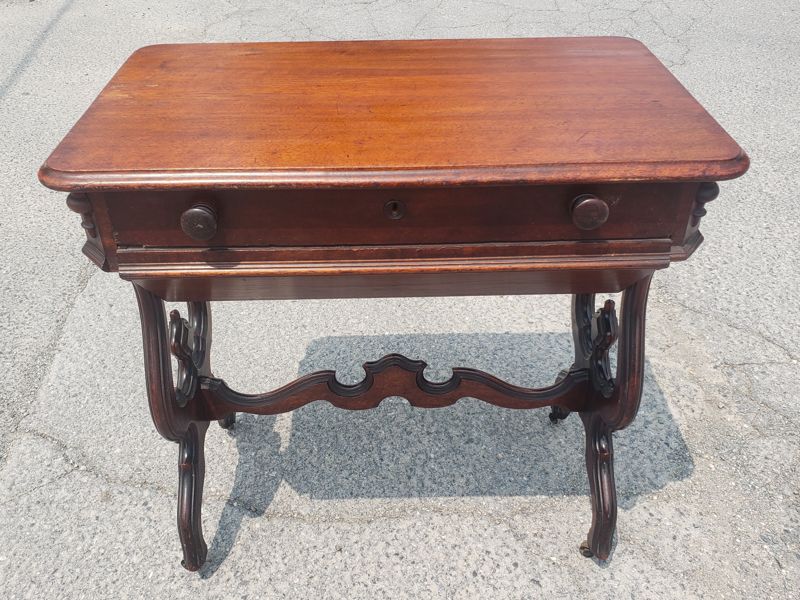 A 19th Century Victorian Rococo Style Carved Mahogany Sewing Table on wheels with a compartmented top drawer and large storage lower drawer.  Very good antique condition. 