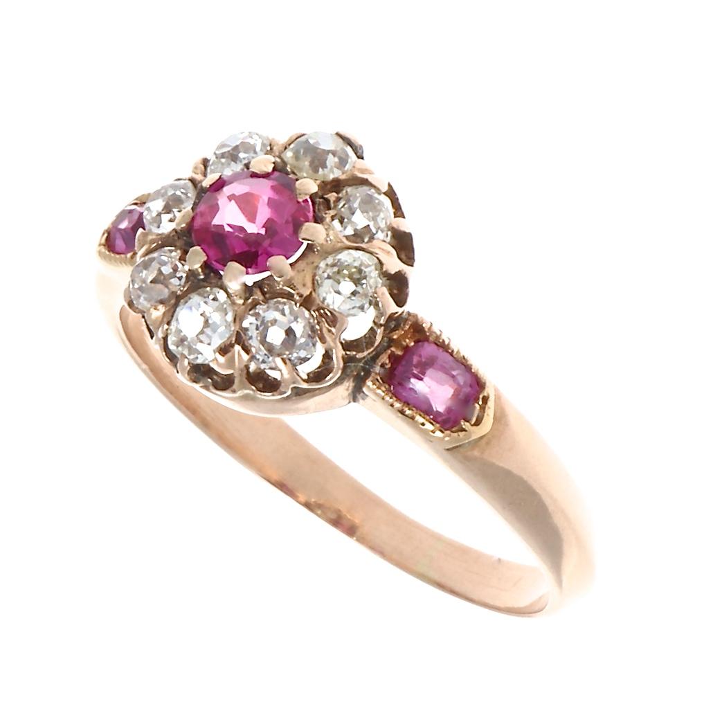 A delicate Victorian cluster ring with rubies and diamonds to delight and inspire. A 0.25 carat round faceted ruby is surrounded by eight old European and old mine cut diamonds that are H-I color and SI clarity, 0.45 carats total weight, and side