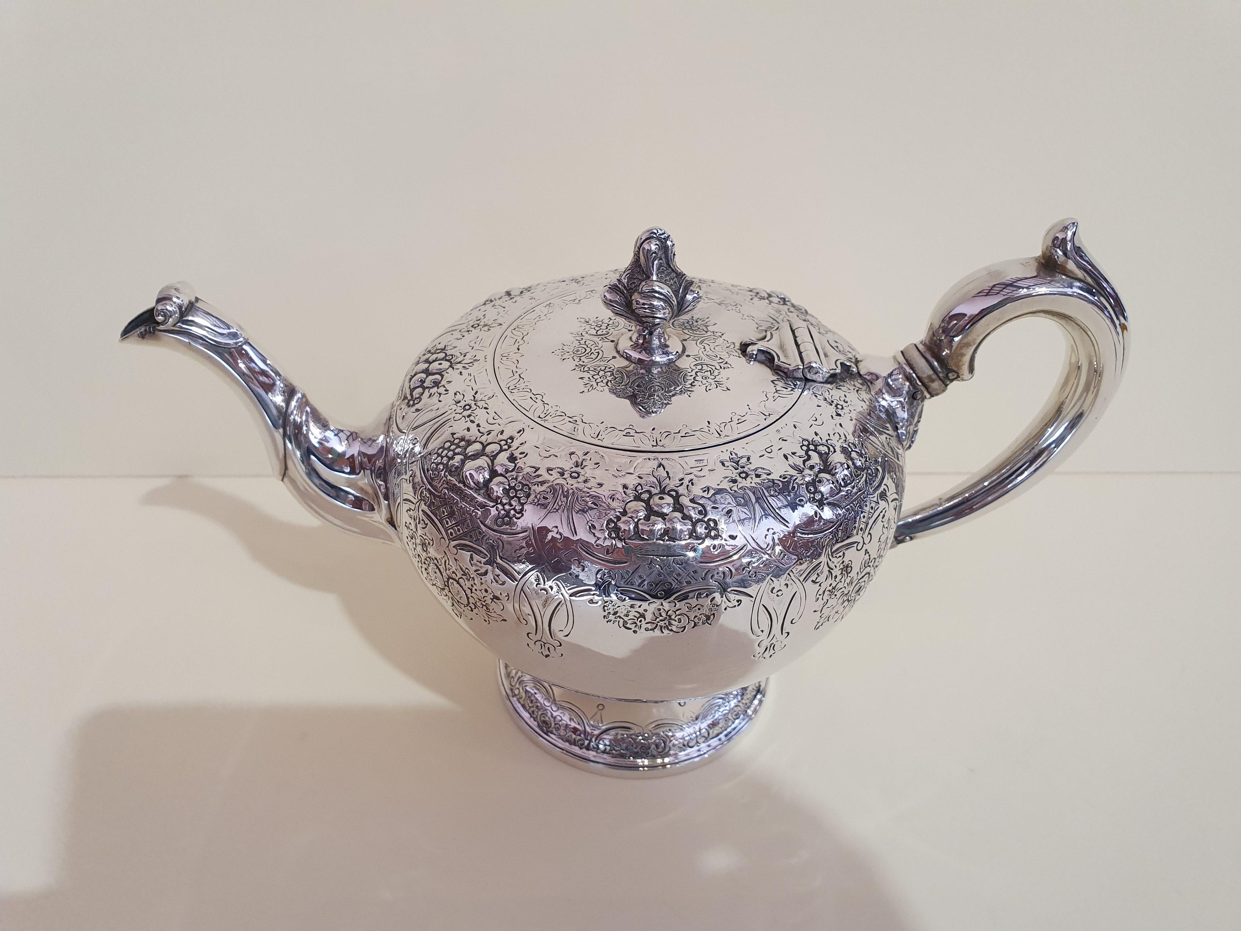 A fine and impressive antique Victorian Scottish sterling silver teapot.
The upper part of the teapot and the cover are embellished with a decoration made with engraving of flowers and embossed fruit baskets.
The engraving is also repeated in the