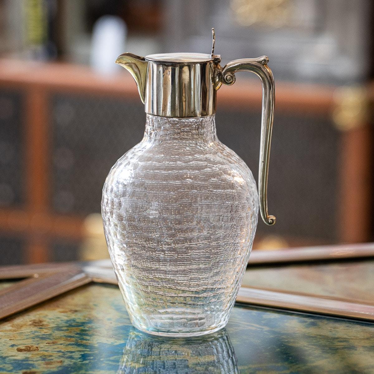 19th Century Victorian silver & cut glass wine jug, the baluster body beautifully hand engraved imitating a hand hammered effect, the plain solid silver collar mounted with a hinged lid, elaborate thumb-piece and an elegant plain scroll