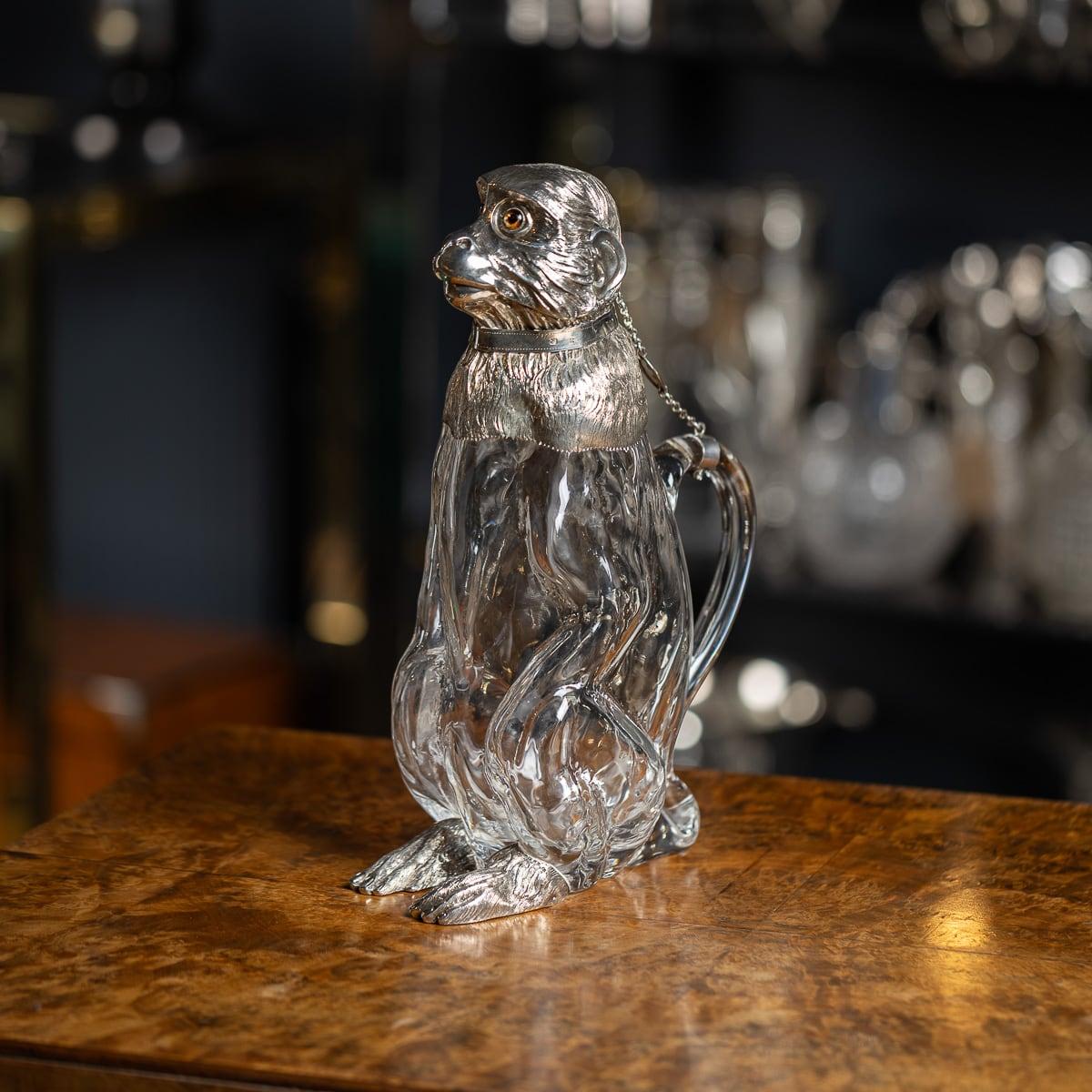 Antique 19th Century Victorian solid silver & glass monkey shaped claret jug. The jug features a meticulously crafted glass body, shaped to resemble a seated monkey, with its front paws resting on its haunches and its tail gracefully curling upward