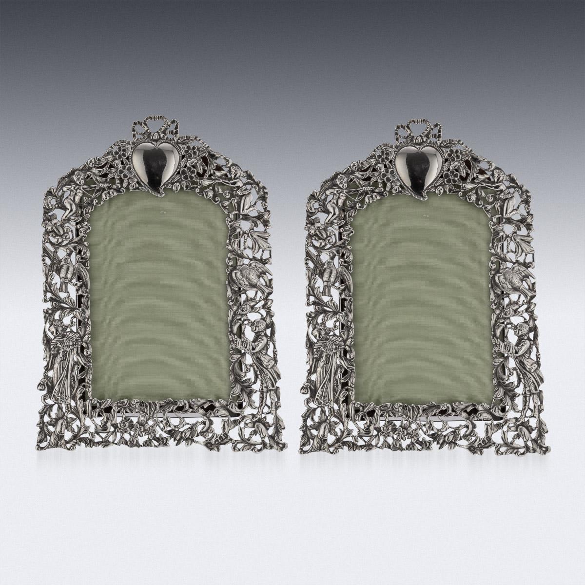 19th century Victorian pair of silver photograph frames, of arched rectangular form with pierced figural, birds and putti in a foliate surround, surmounted by a heart-shaped cartouche, glazed central aperture with green silk lining, on a hardwood