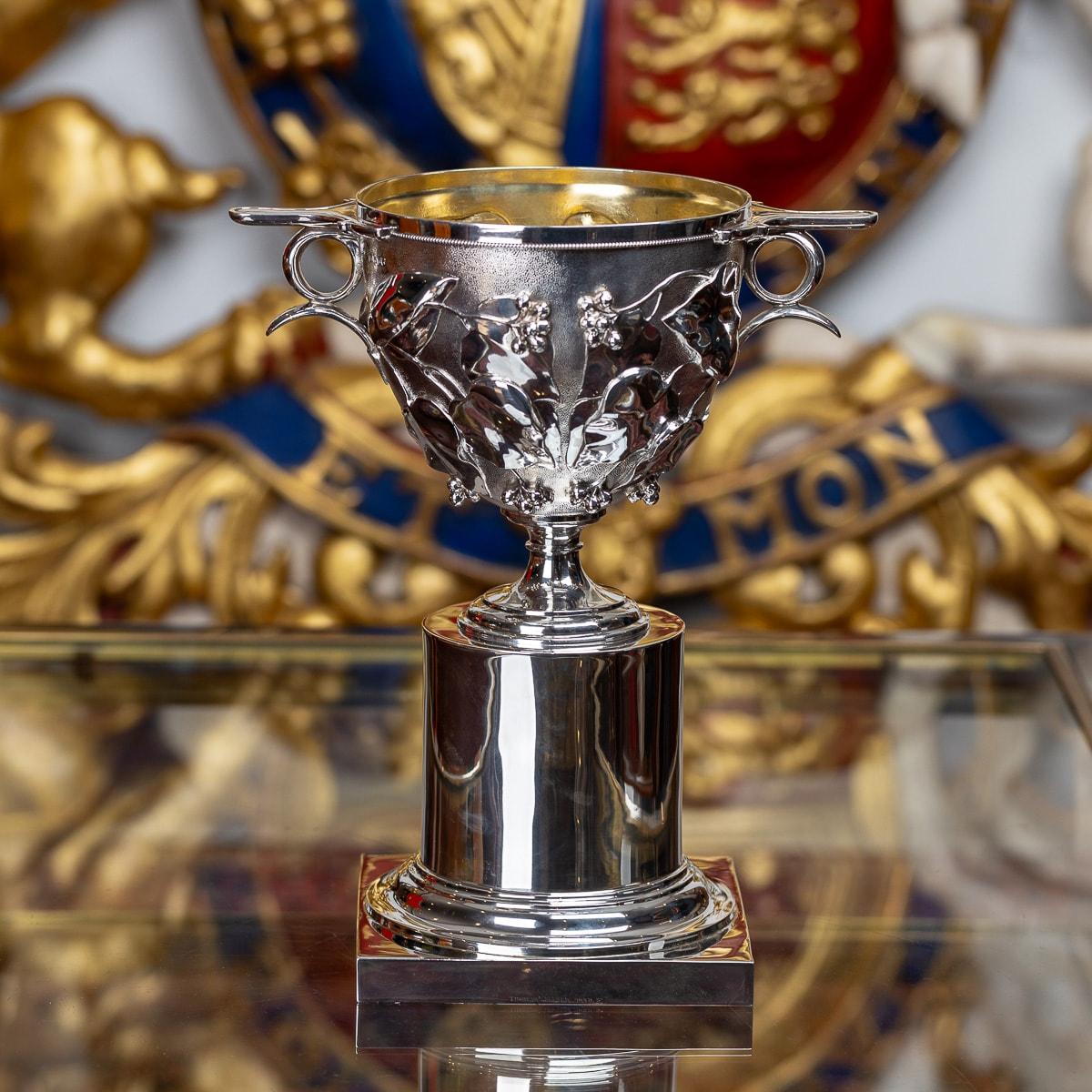 Antique 19th Century Victorian solid silver skyphos cup, of traditional form on a plane columb base, of heavy gauge and the body chased with holly leaves and berries on matted ground, flat handles with rings beneath, on a tapering foot and richly