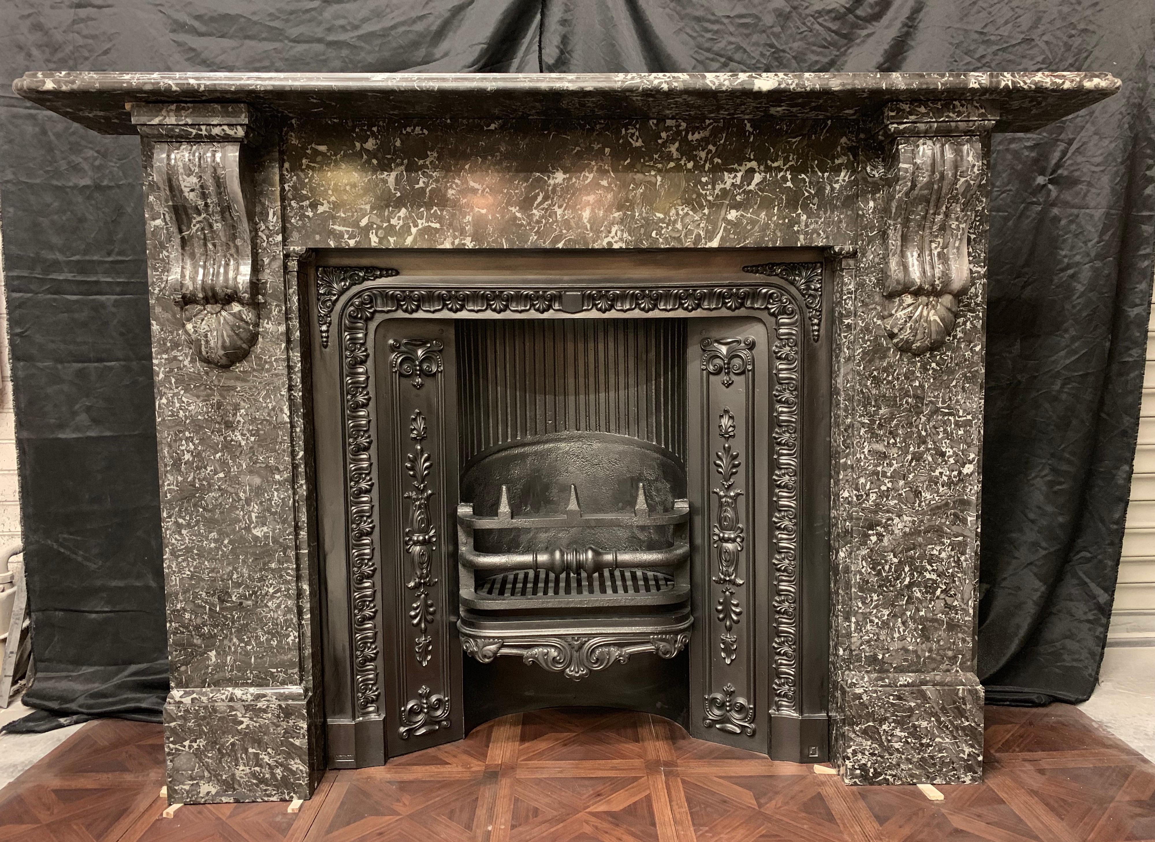 A large and regal 19th century victorian fireplace surround in charcoal grey St Anne's marble, A deep moulded shelf sits directly above an unadorned frieze resting on moulding and block supports flanked by stepped jambs hosting large and well carved
