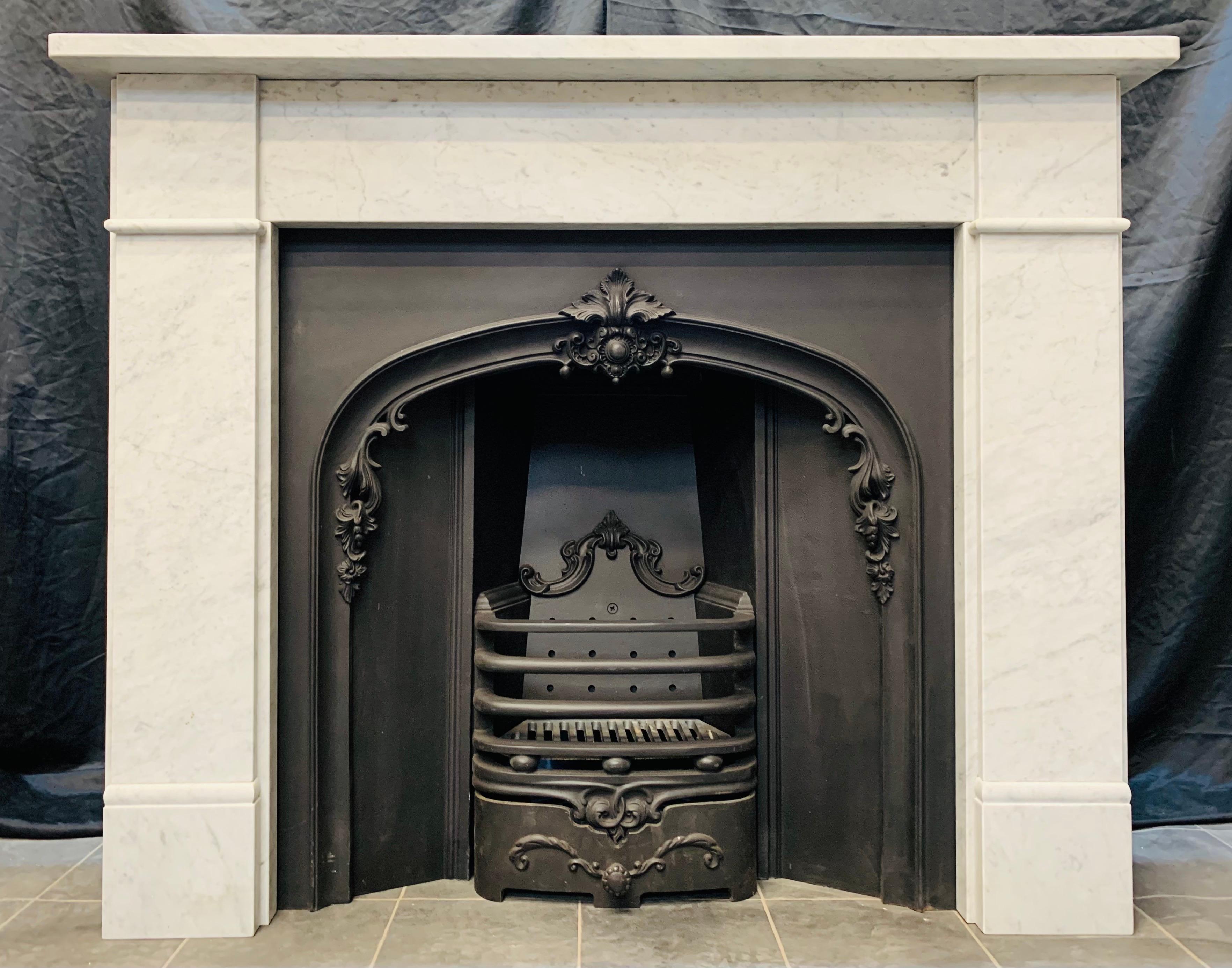 An unadorned 19th century Victorian style Carrara marble fireplace surround. A square shelf sits above a plain frieze, flanked by stepped jambs with a separation moulding to the frieze line, all resting on moulded foot blocks. 

1900c English.