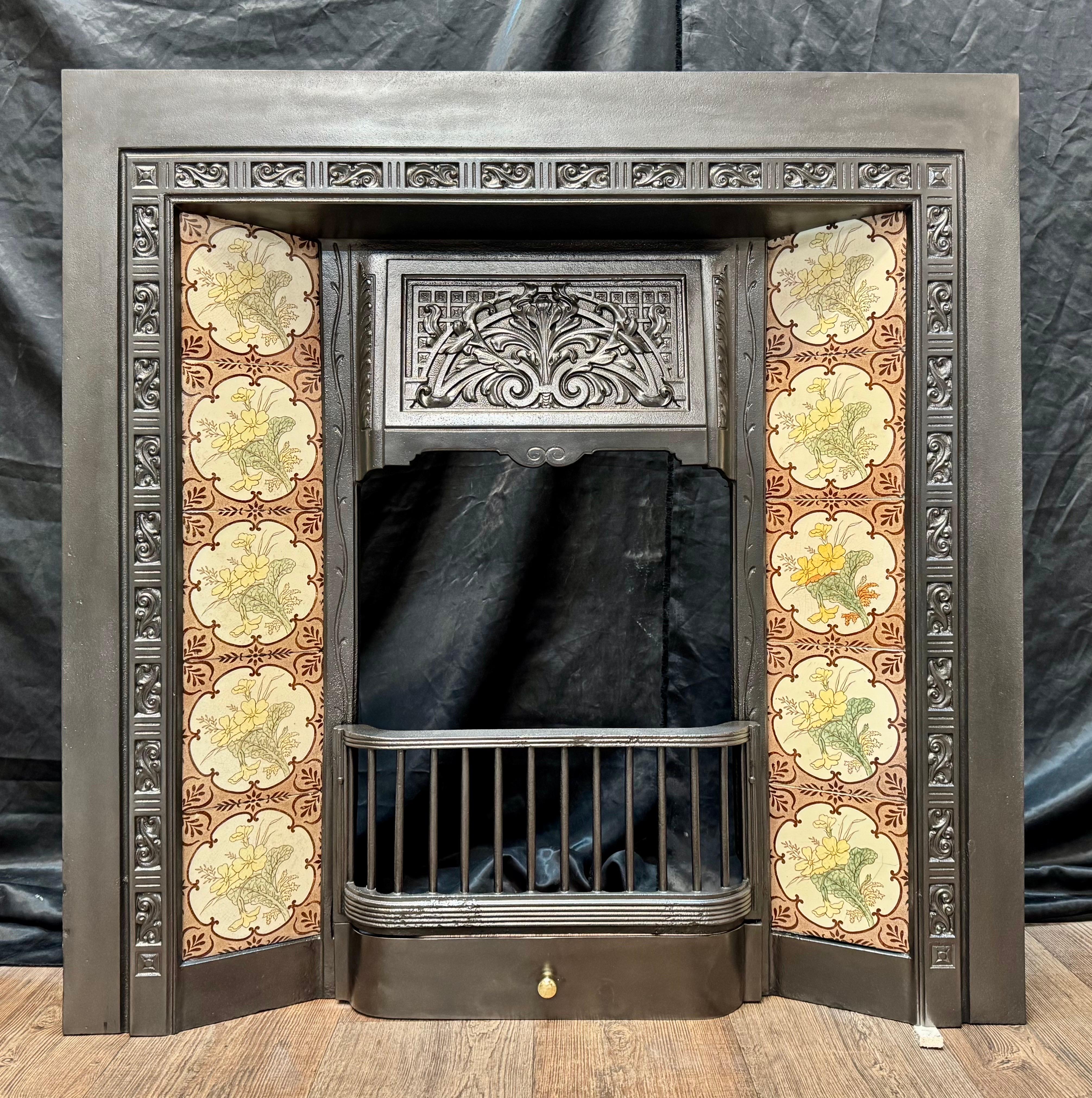 A Late 19th Century Victorian cast iron fireplace insert with its original tile set. 
A generous outer frame, with a raised cast border, two sets of hand painted tiles showing spring flowers. Central to this piece is a high relief cast hood with