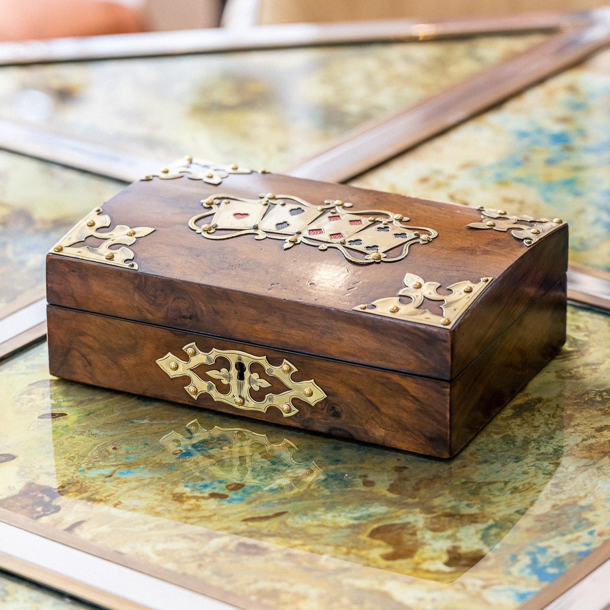 Ancien compendium de jeux en noyer de la fin du 19e siècle de l'époque victorienne. La boîte elle-même est protégée par une serrure et une clé, le couvercle étant orné de cartes à jouer décoratives en laiton, entourées de décorations d'angle dans le