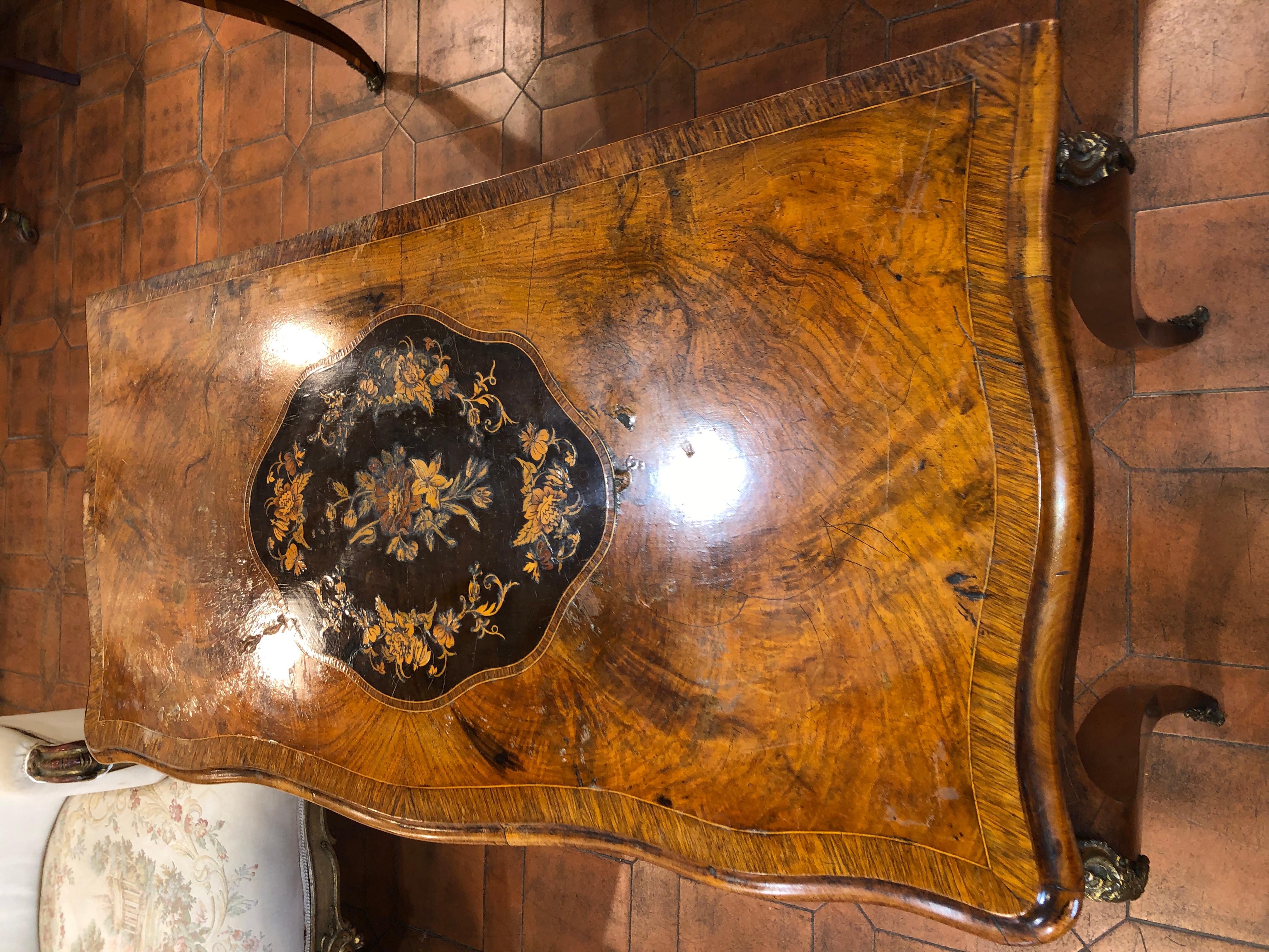 Gaming table from the English Victorian era, in walnut root and inlaid in fruit woods, saber-shaped legs, with applications in gilded bronze. The game table resumes French forms and style but in a way less rich in bronzes and inlays. To be restored