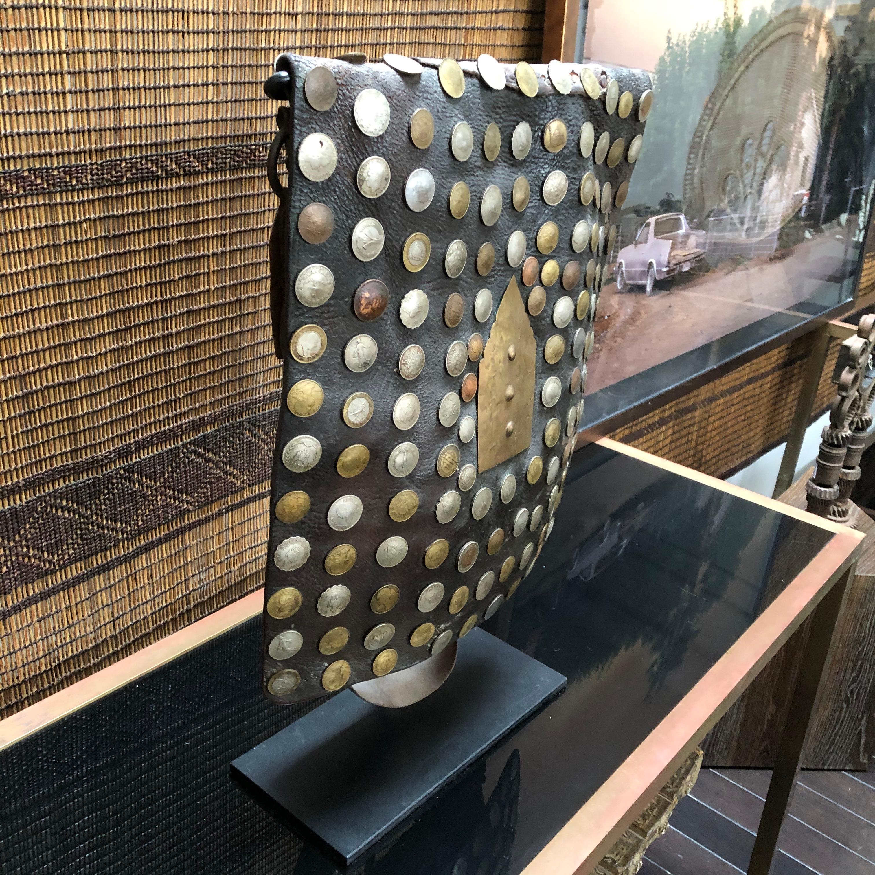 A vintage handcrafted leather water carrier bag from Morocco on a stand. Handmade with camel hide and decorated with antiqued coins from around the world. 

Traditionally made for water sellers in order to carry water through markets and sell to