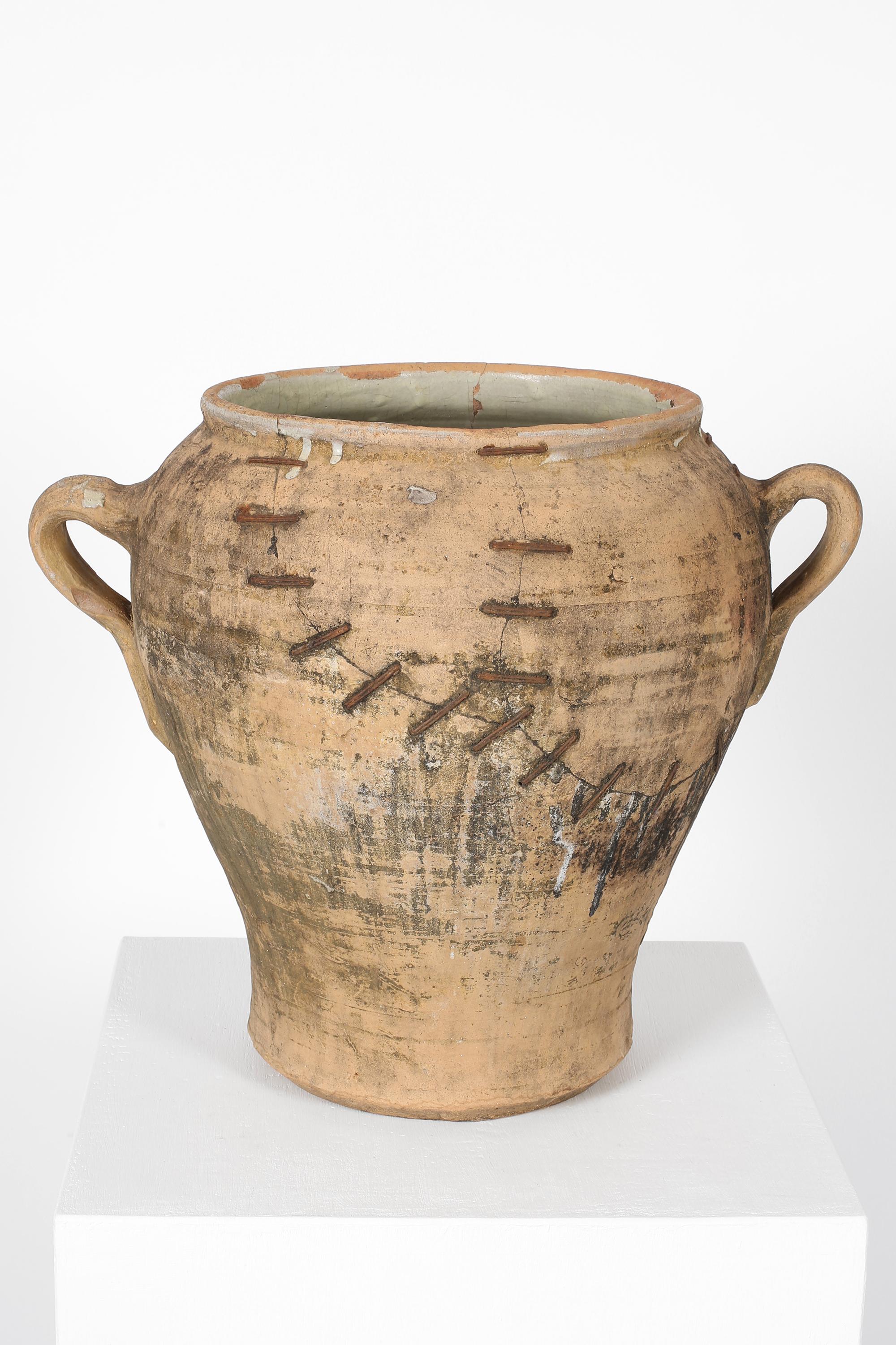 Un recipiente in terracotta, fortemente patinato e lavorato a mano, con due maniglie e molteplici riparazioni con graffette di ferro. Dalla provincia di Siviglia, in Andalusia. Spagnolo, 1870 circa.