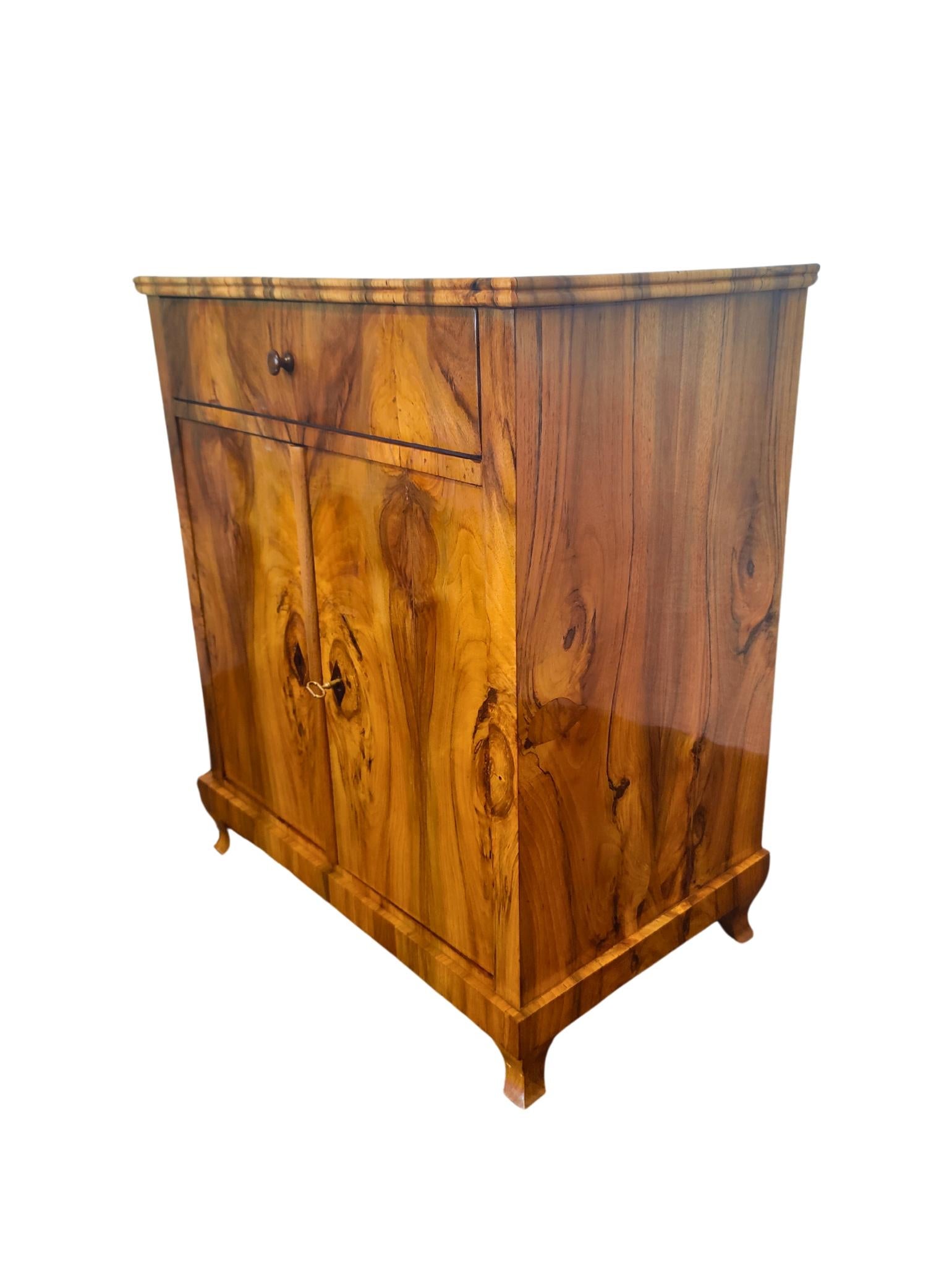 Small, fine Biedermeier half cabinet in walnut veneer. The veneer is continuous and partially mirrored. Very nice little piece of furniture with 2 doors and a drawer at the top. 
In very good restored hand polished condition. 