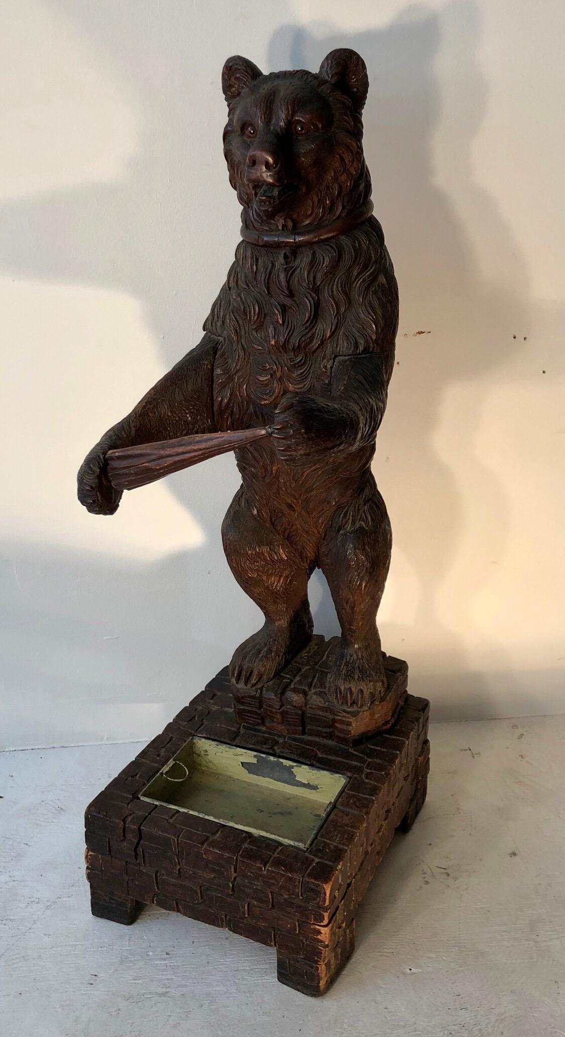 This exquisite carved Black Forest bear cane / umbrella stand with glass eyes and is holding a carved umbrella to hold the walking sticks. The Bear is standing on a faux stone plinth carved out of wood with its original drip tray.