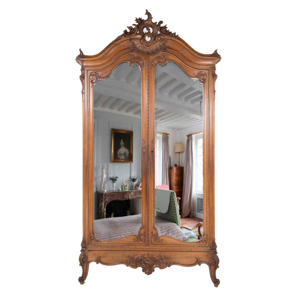 A French highly-carved two-door Louis XV style walnut armoire, the crown with dramatically-carved crest and corner details.
Retaining their original curved hand-bevelled mirrors, the doors are further embellished with carved details around the