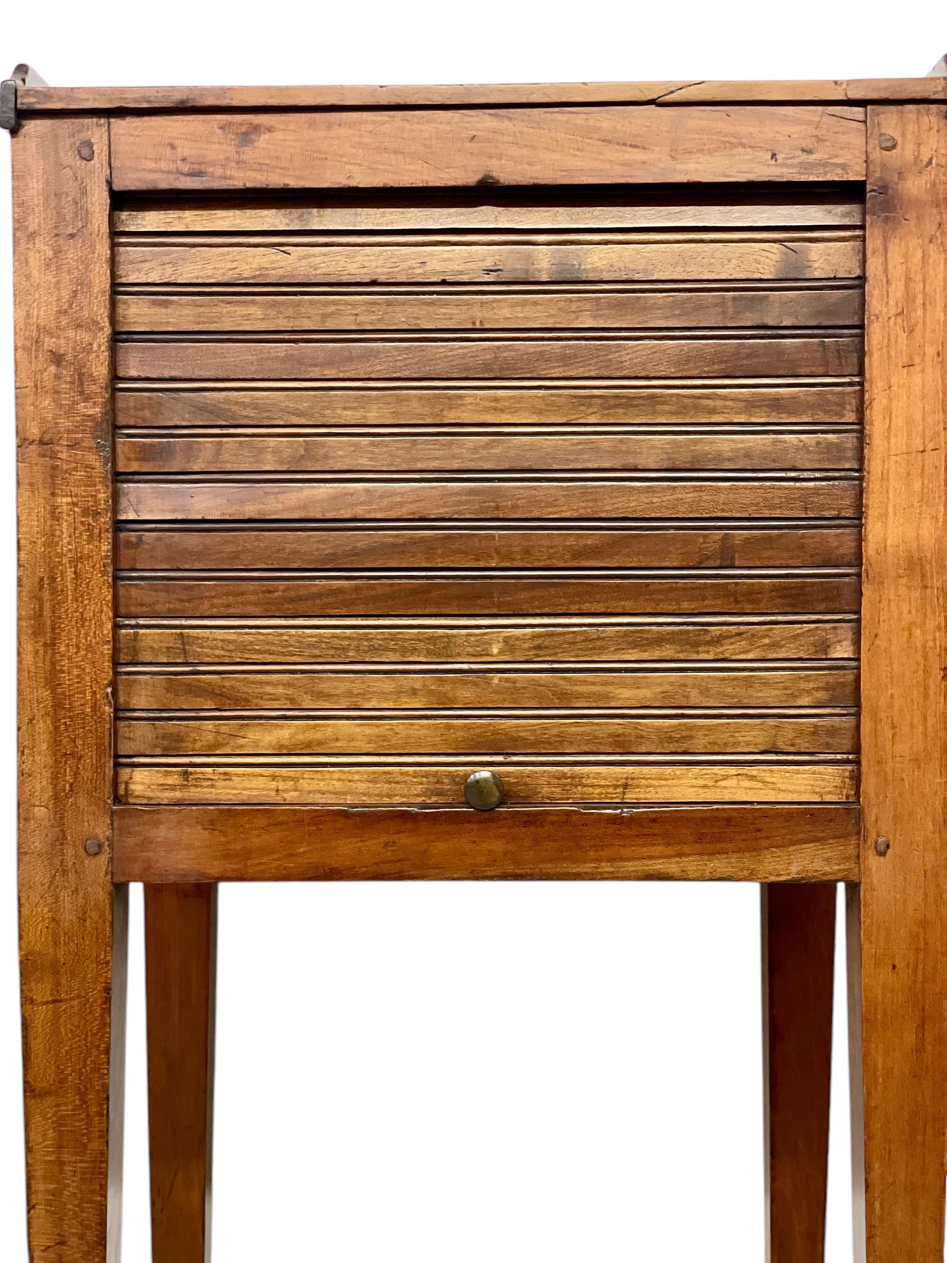 This charming, mid-19th century nightstand is a wonderful example of rustic craftsmanship. Crafted entirely from solid walnut, this petite piece exudes warmth and character. The nightstand features a unique sliding shutter, composed of rounded slats