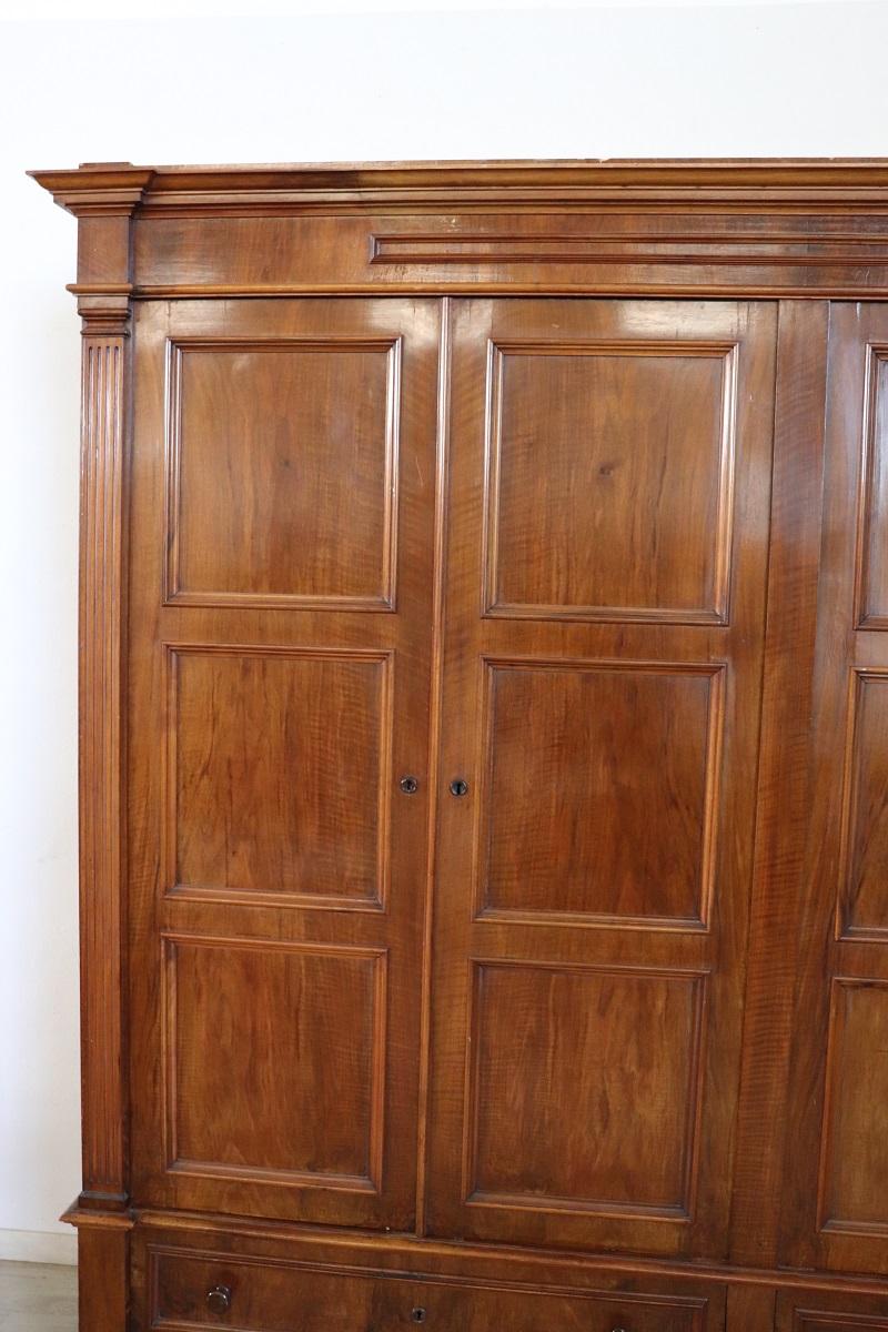 Antique italian wardrobe in solid walnut wood made in late 19th century. This truly spectacular wardrobe is very rare due to its large dimensions equipped with four doors. The interior is equipped with three solid shelves for each part. In the lower