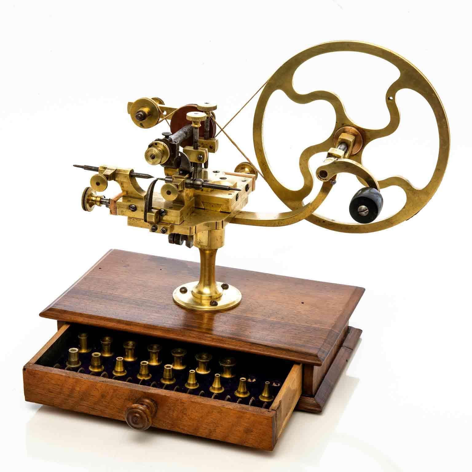 A rare gear wheel rounding up machine for watchmakers, machine à arrondir ingenuous watchmaking machine used to true up watch wheels and shape gear teeth, mounted to a walnut box with frontal drawers containing accessories, two missing. 

This