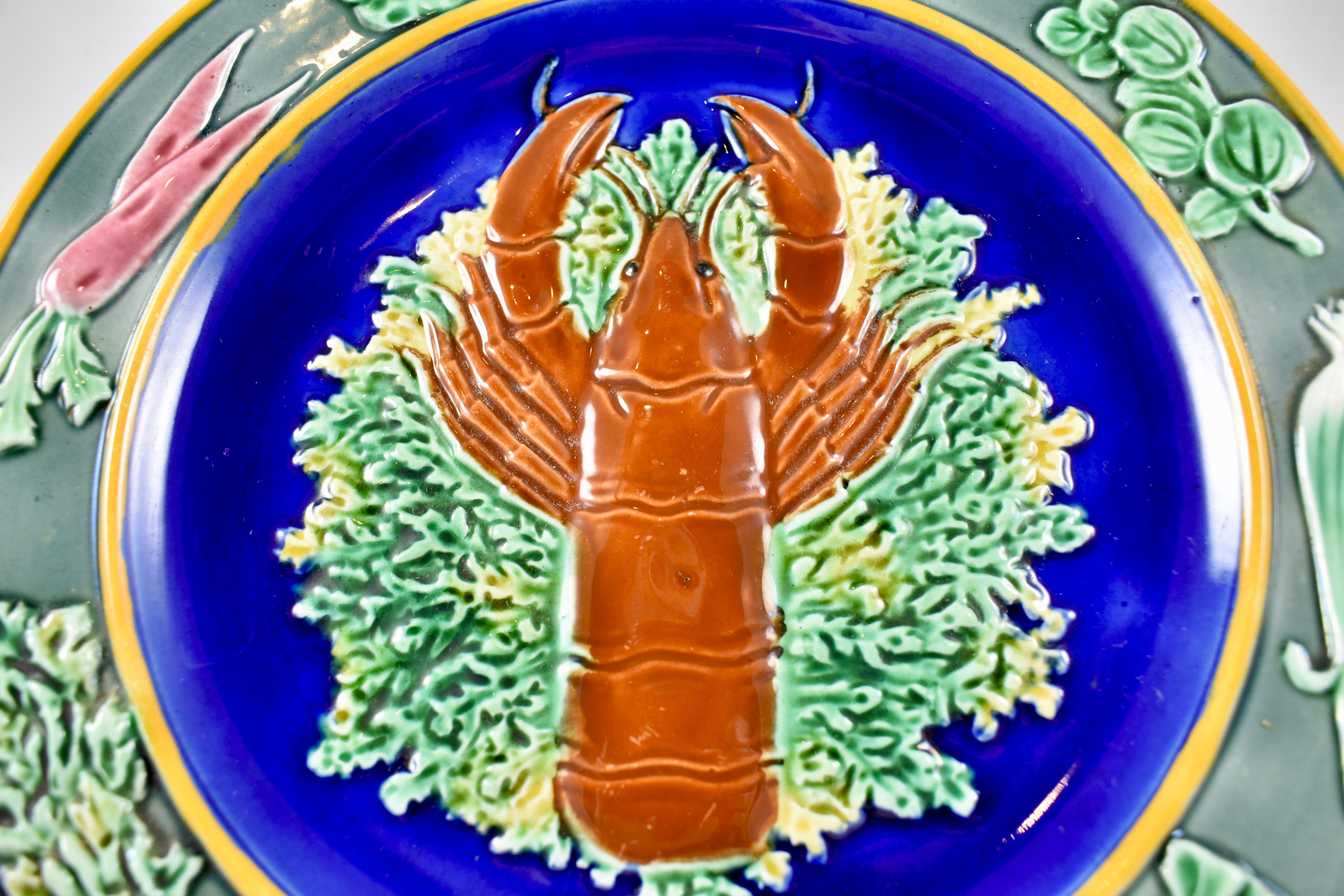 In the Aesthetic taste, a Wedgwood majolica plate, a center well showing a lobster on bed of yellow and green seaweed against a Cobalt blue ground. The outer rim is dotted with raised root vegetables, radishes, carrots and leeks, along with their