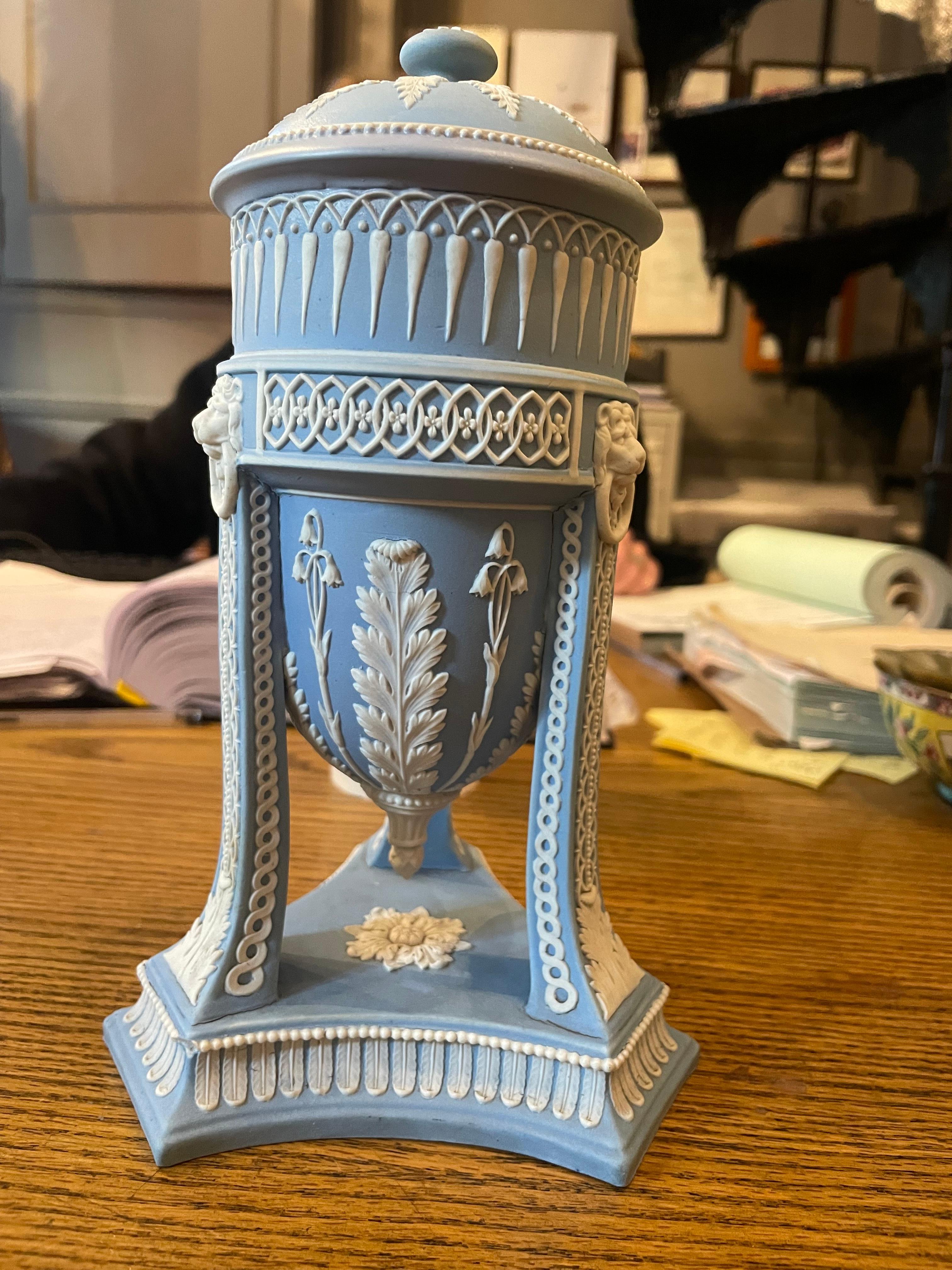 19th Century Wedgwood light blue Jasper tripod vase complete with cover with applied white relief of foliage and bell flowers, the terminals with lion masks and rings, all standing atop a triangular base.
