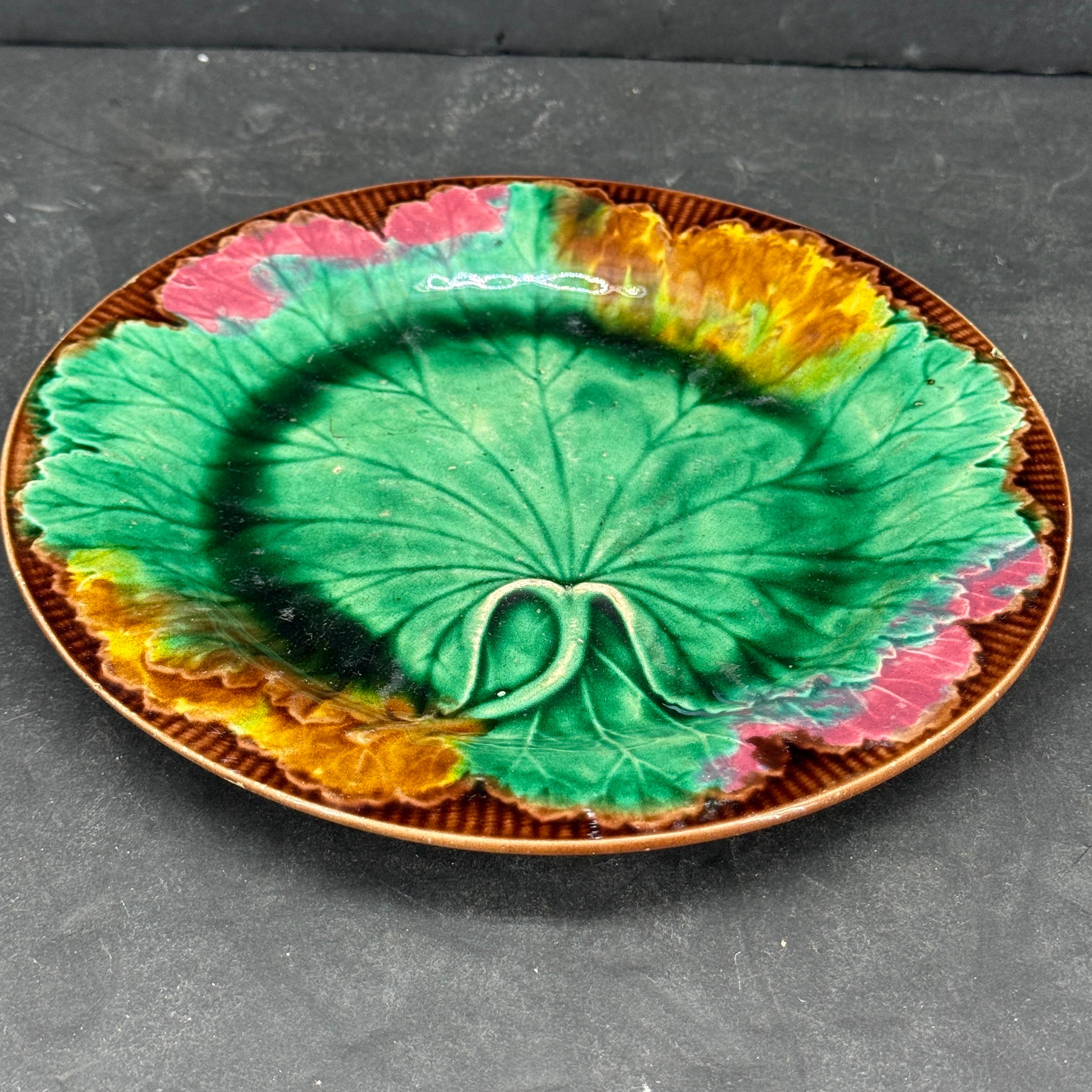English Wedgwood Majolica Ceramic Cabbage Leaf Plate. Highly collectable Majolica plate moulded with a cabbage leaf design, on a basket weave background and then this is covered in green, red, brown and yellow glazes. The plate has two initials on