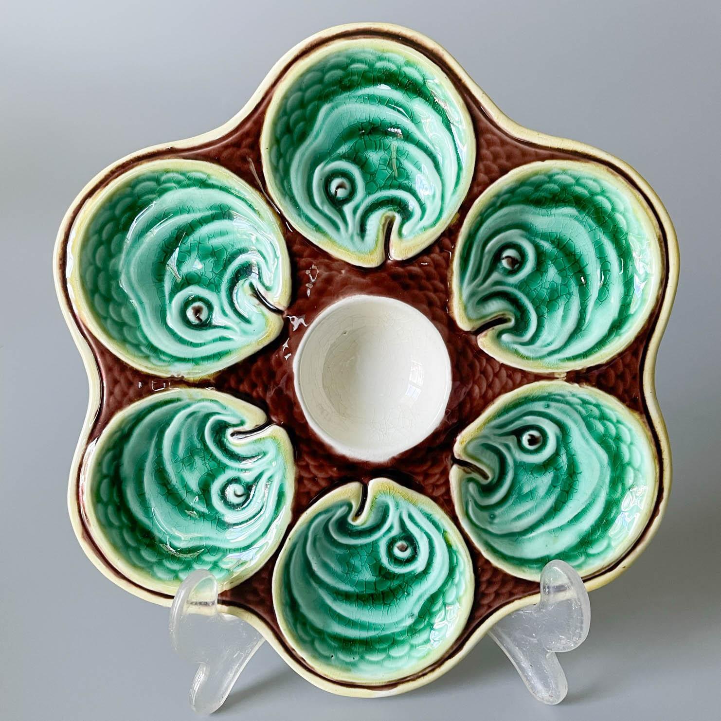 A small 19th century English Wedgwood majolica oyster plate having six wells with green fish head motif surrounding a central white well. Brown ground molded as fish scales with yellow as an accent color. Stamped Wedgwood to the underside. Circa