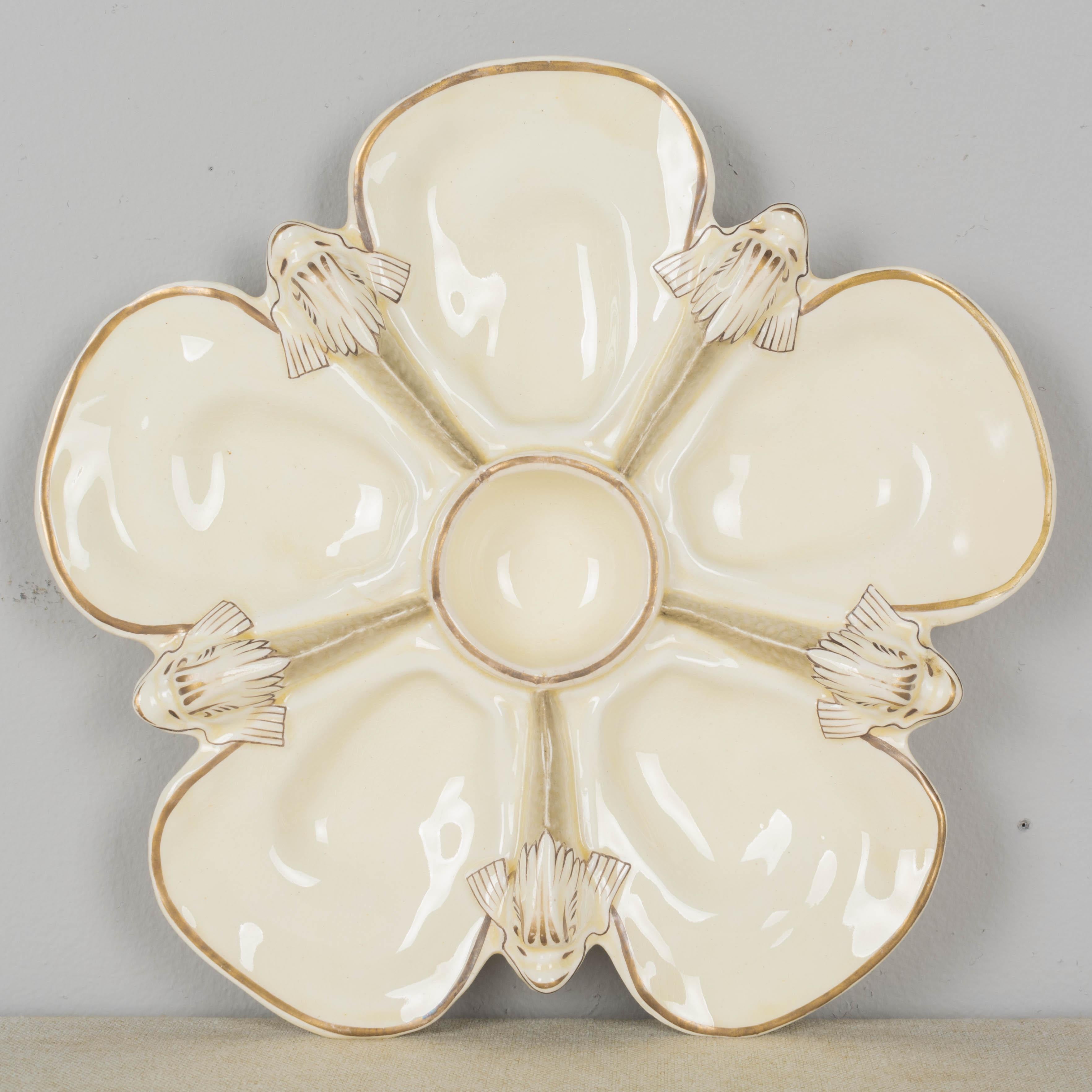 A 19th century English Wedgwood majolica oyster plate, with five oyster shell wells, central well for sauce and five molded dolphins separating each. Light cream color glaze with pale gilt trim. Impressed mark on reverse. Small chip to foot on
