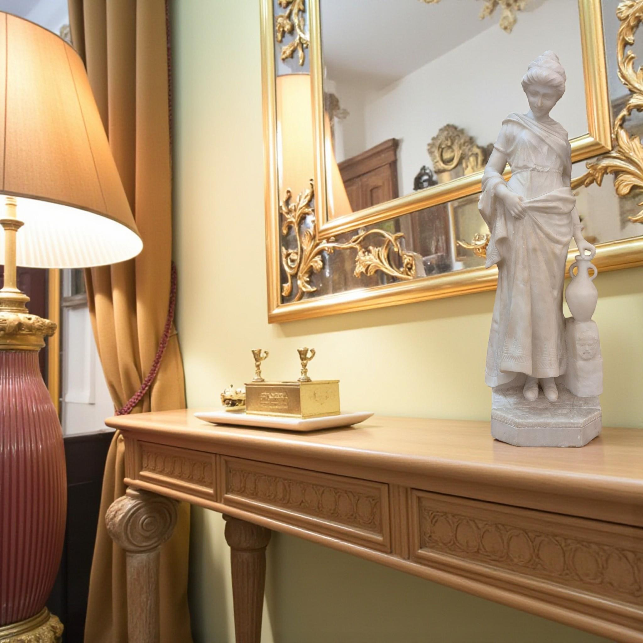 Questa squisita scultura in marmo bianco di Carrara del XIX secolo raffigura una giovane donna graziosamente drappeggiata che tiene in mano una brocca, che poggia su una fontana ornata da un volto ispirato all'iconica Bocca della Verità. Questo