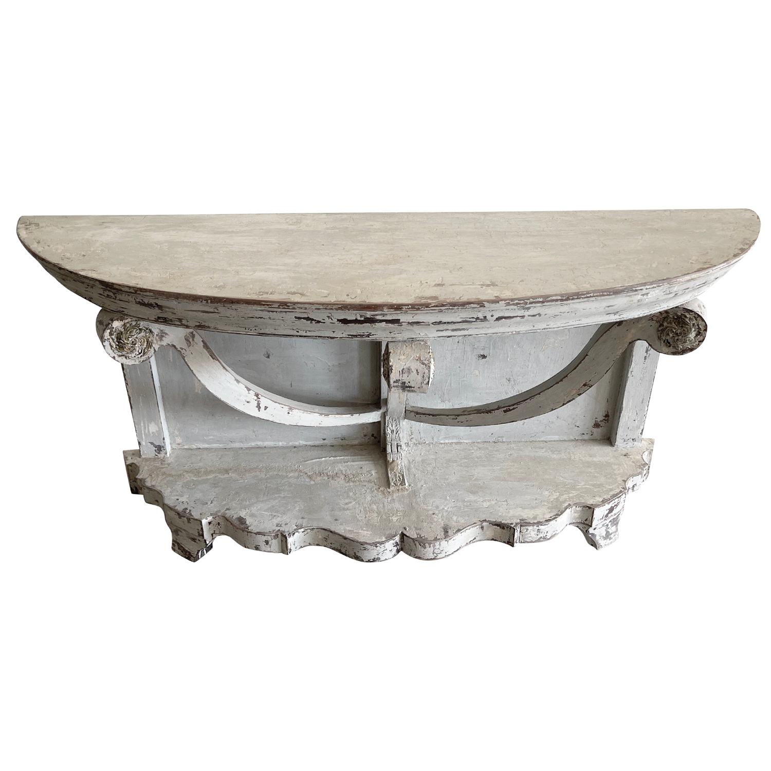 An antique 19th Century Provincial demi-lune console table with crown molding is decorated and supported by large swags, in good condition. The wall mount console is resting on a heavy bottom shelf. Hand crafted in painted Oakwood with the original