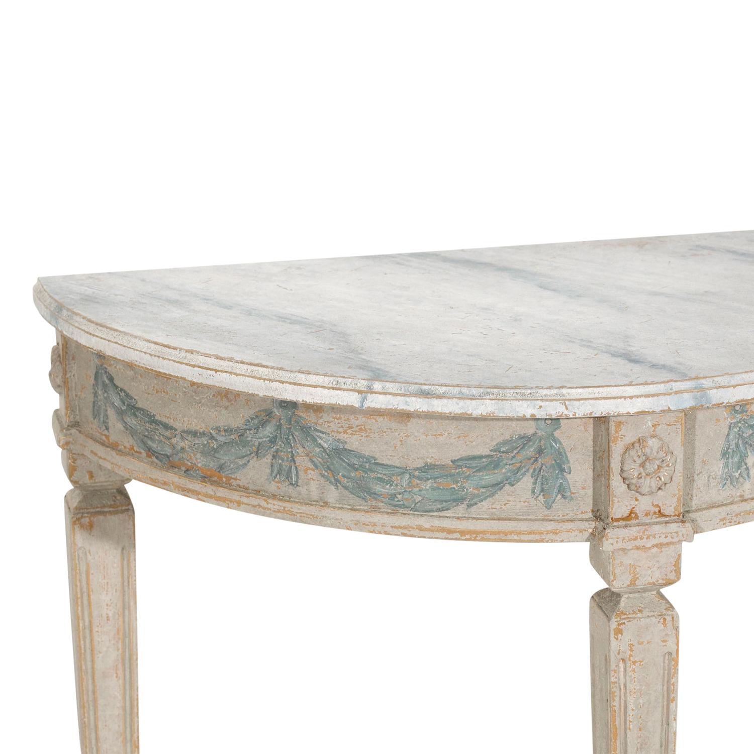 A light-grey, white antique Swedish Gustavian pair of small console tables made of hand crafted painted Pinewood, in good condition. The detailed freestanding demi-lune tables are enhanced by detailed blue floral carvings, standing on three long