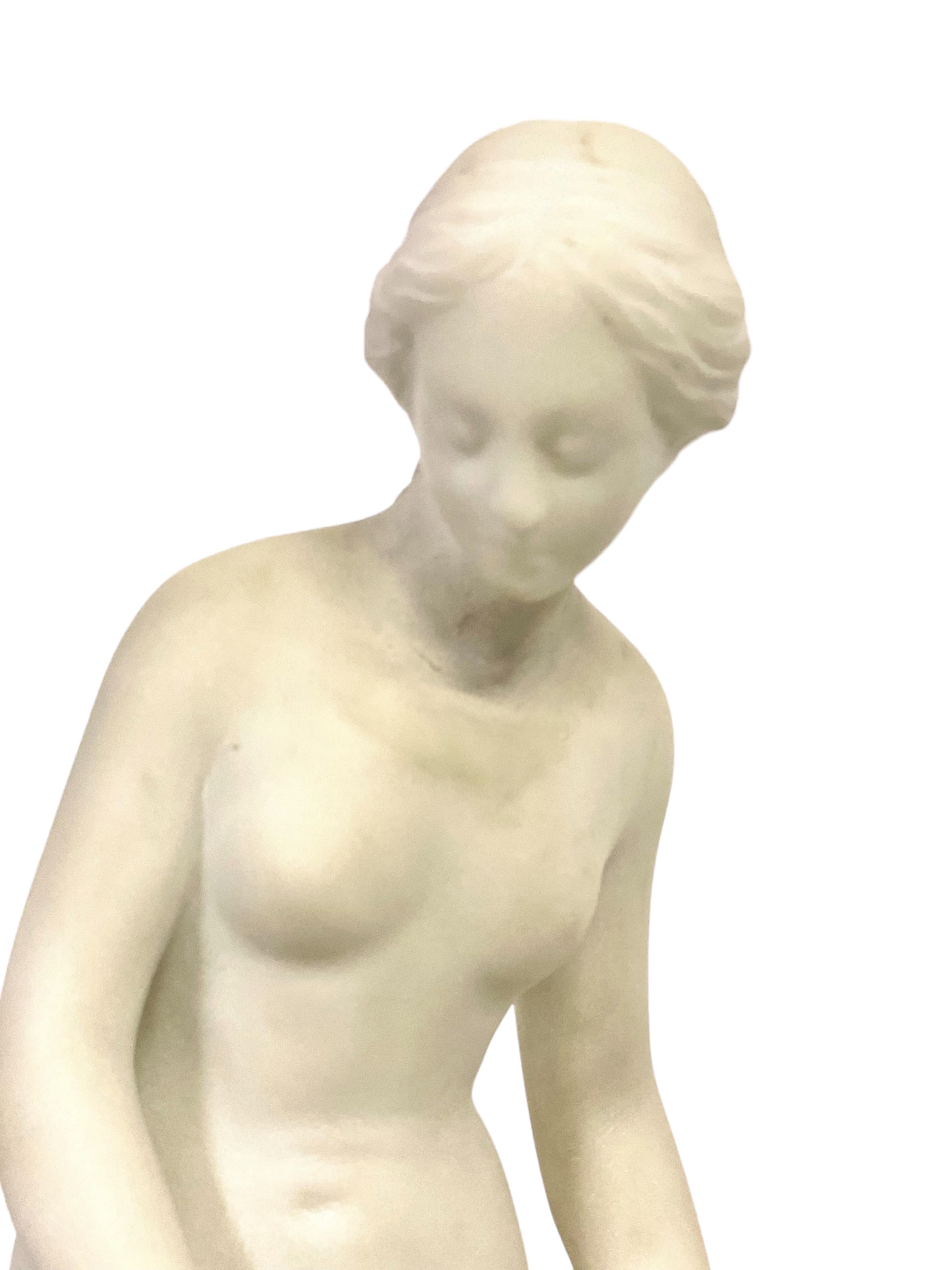 Charmante sculpture en marbre blanc représentant une jeune fille se préparant à se baigner, inspirée du célèbre marbre 