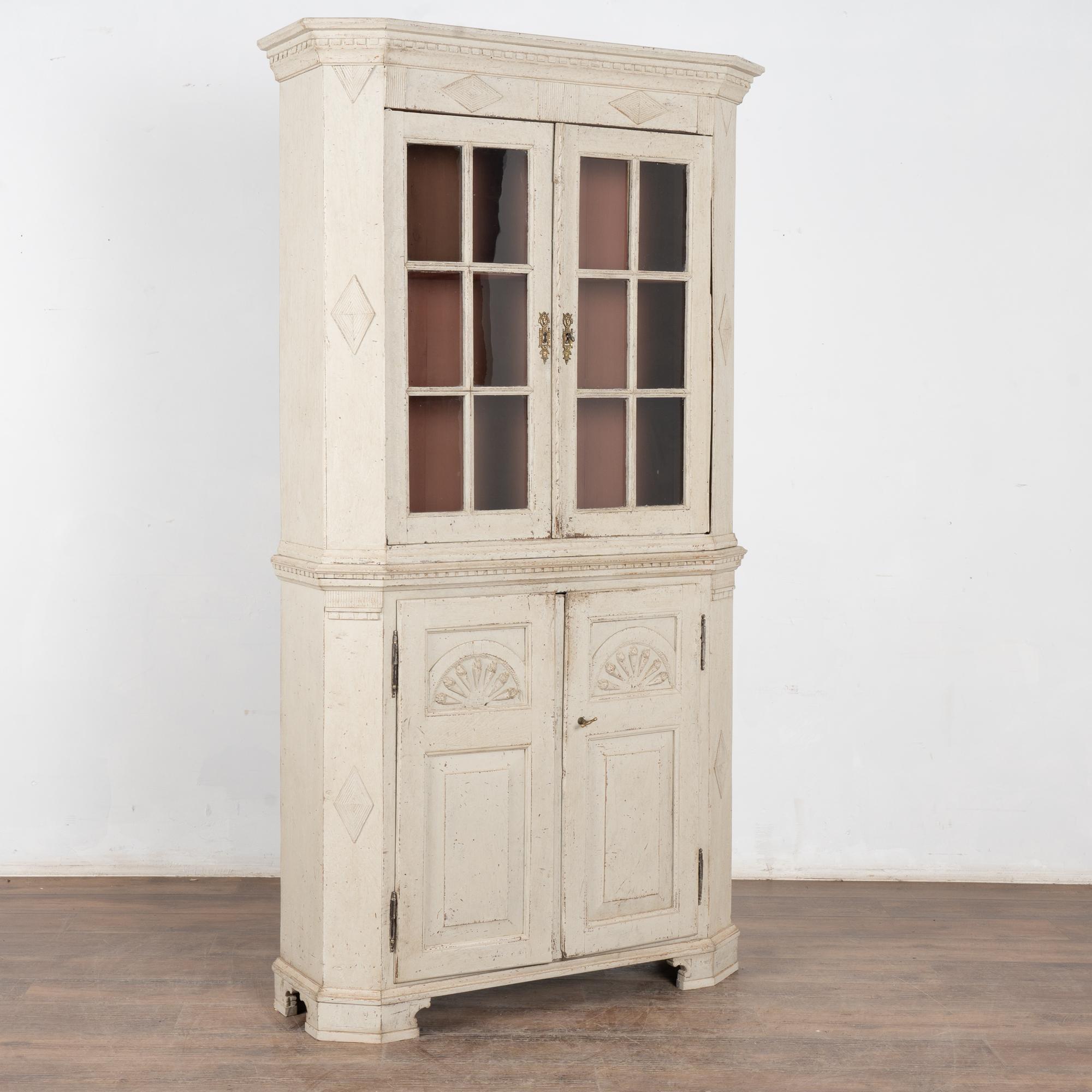 Lovely Gustavian display cabinet with upper pane glass doors. Traditional carved diamonds, dentil molding, and additional carving add to the timeless appeal of this bookcase.
The exterior antique white painted finish is old and shows distress