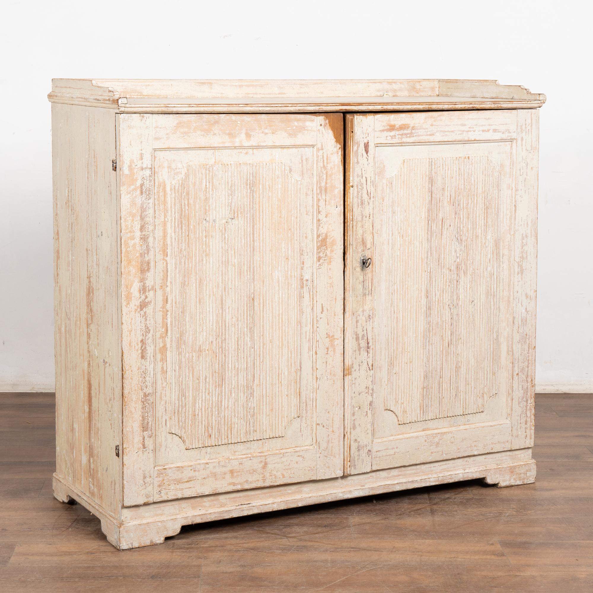 This lovely Gustavian sideboard comes from the Swedish countryside. The simple fluted carving along the panel doors was a traditional element in Swedish furniture from this era.
The original antique white painted finish (may also appear light gray