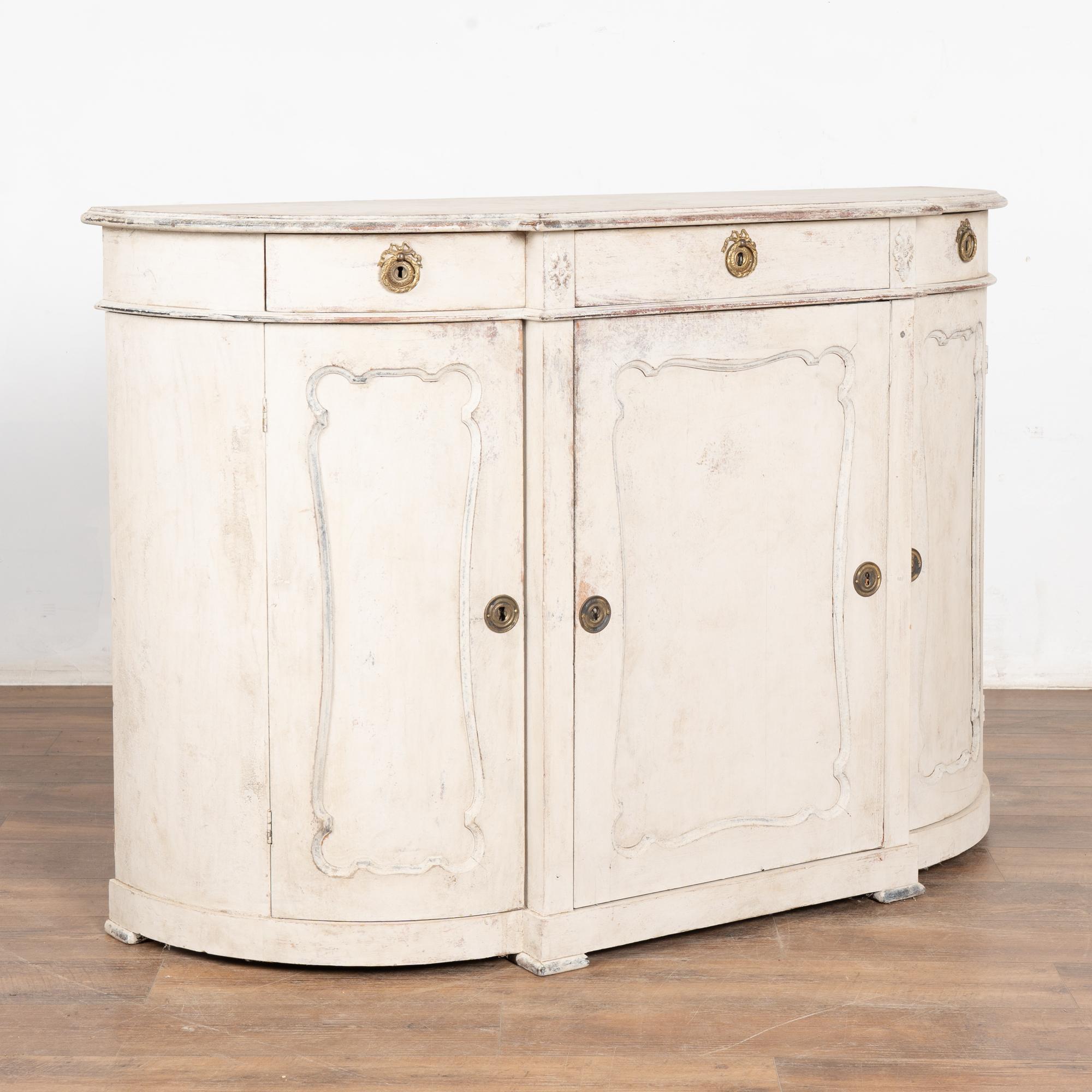 Swedish Gustavian painted pine sideboard with attractive curved sides and panel details.The curved end cabinet doors make this cabinet a special find.
Later professionally painted in layered shades of antique white (with soft gray accents/undertone)