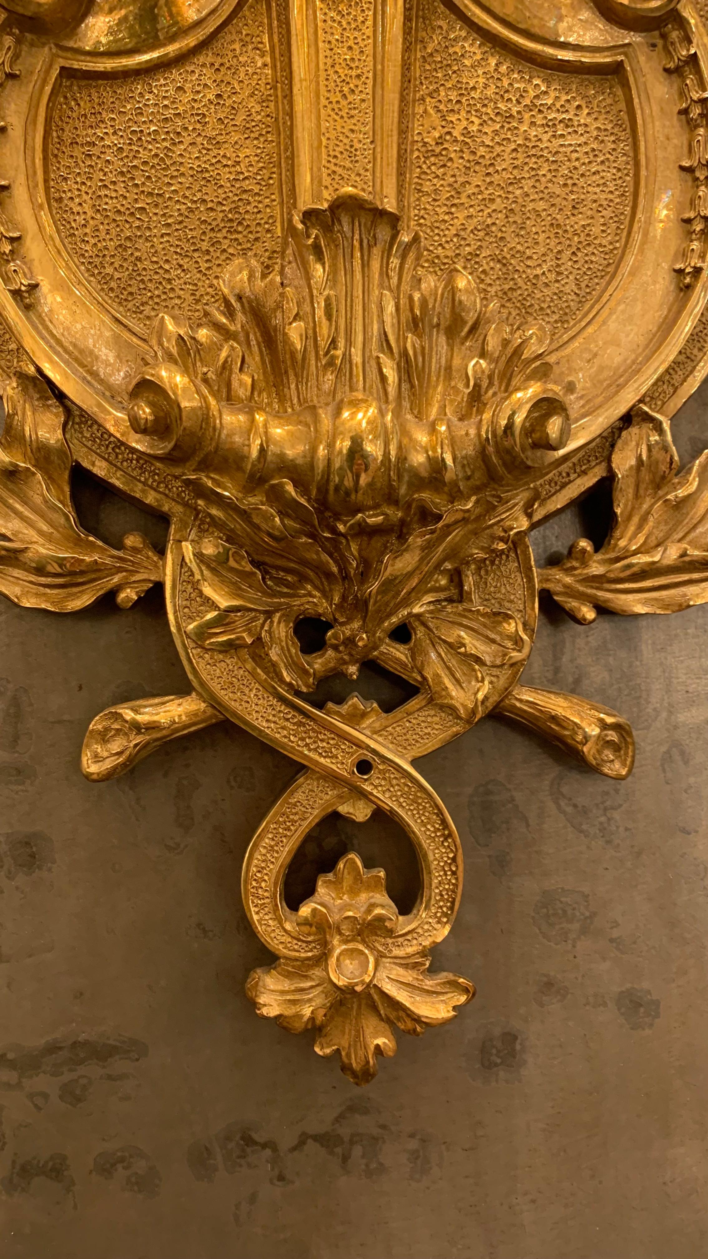 Esta lámpara de pared está inspirada en un modelo de araña de Josef Hoffmann (arquitecto y diseñador miembro de la Secesión vienesa).
En efecto, la parte inferior del candelabro, compuesta por tres hojas de palmera adornadas con gotas, se aproxima