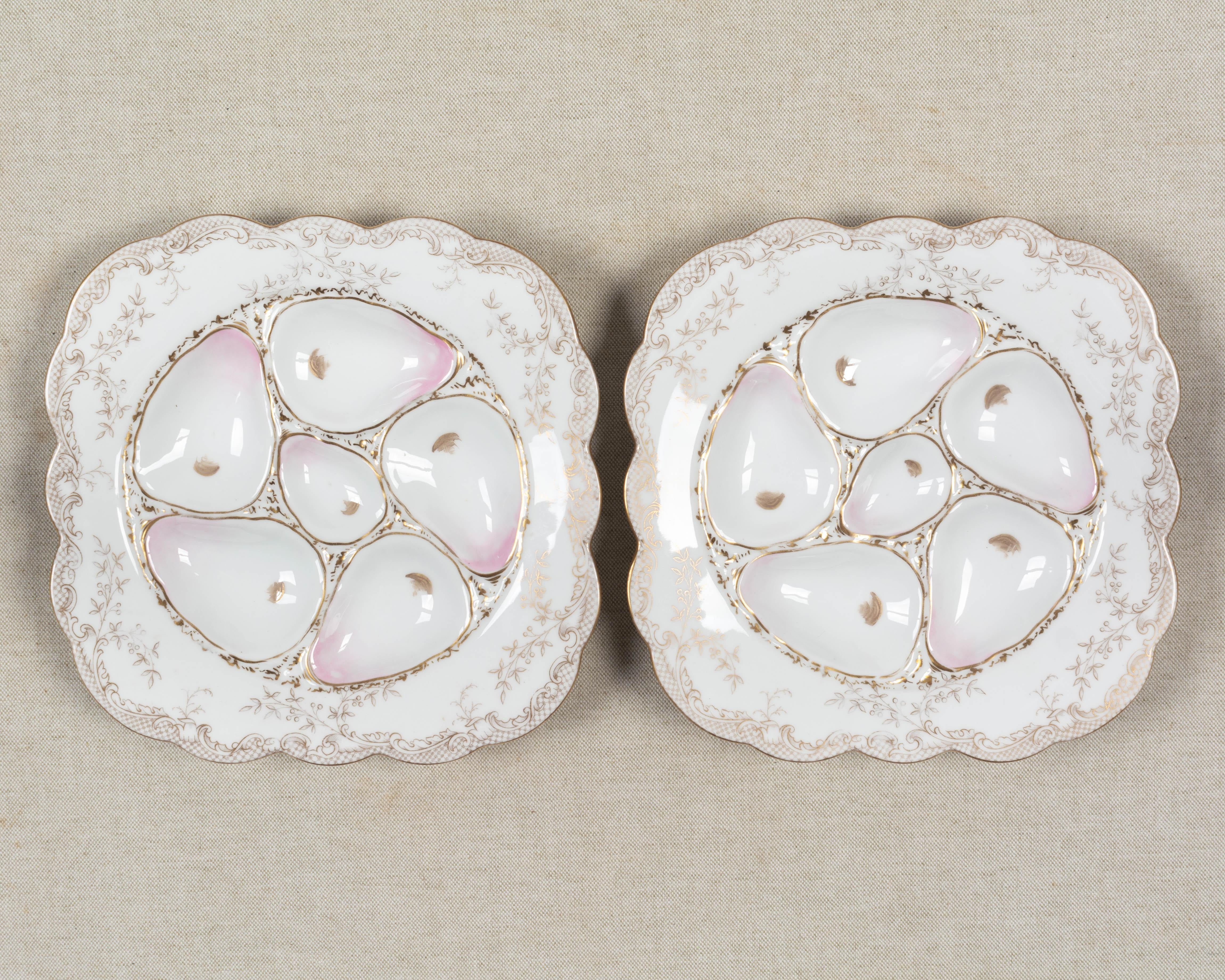 Un par de platos de ostras de porcelana Wilhelm & Graef con cinco pocillos de color rosa pálido y un pocillo central para salsa. Ancho borde cuadrado con delicada decoración foliada dorada. Marca en la parte inferior: Wilhelm & Graef Nueva York