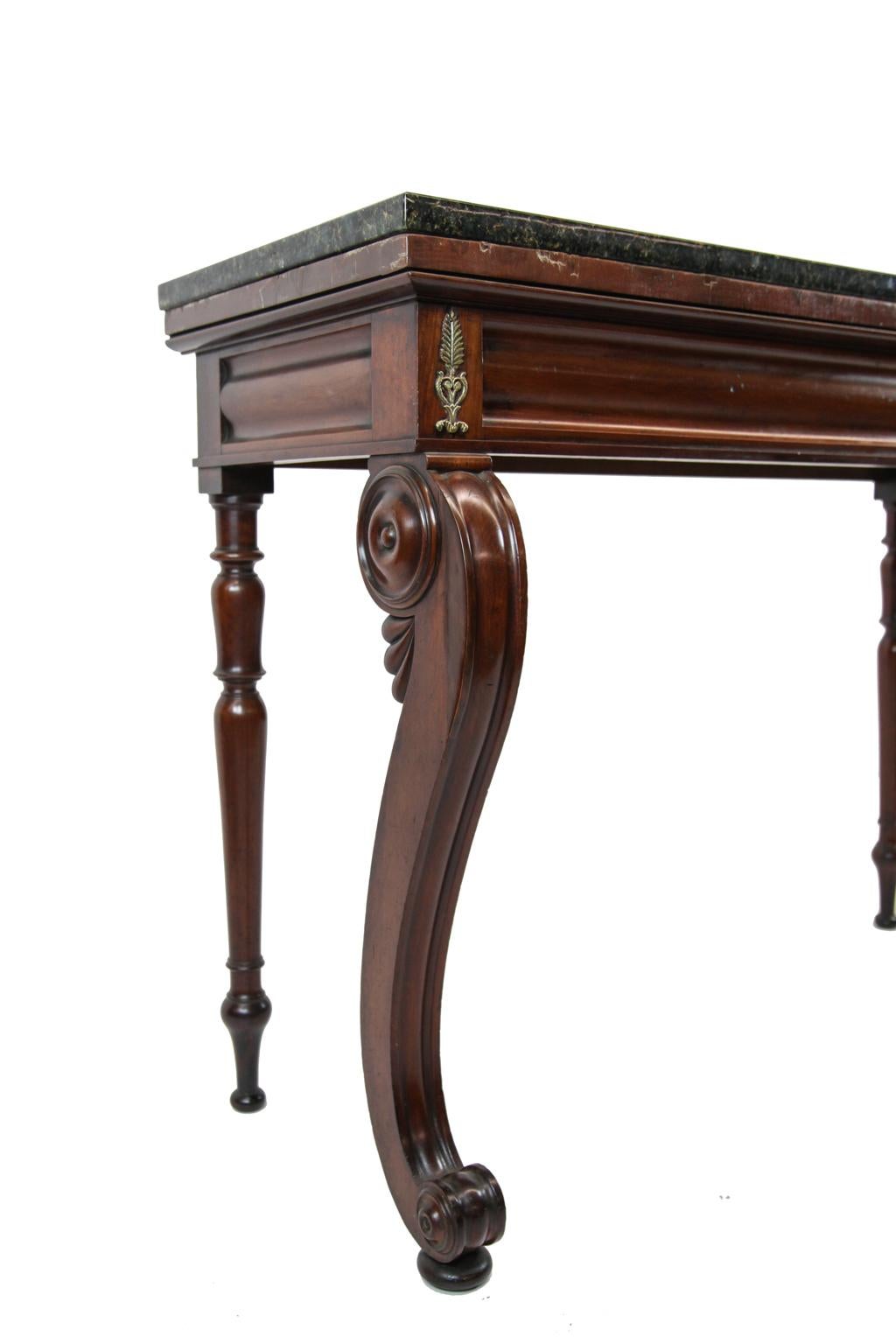 19th century William 4th console table in mahogany, with ubatuba granite top, convex shaped frieze with brass ornaments at the corners, front saber shaped molded legs with large circular medallions on either sides with smaller ones at the feet,