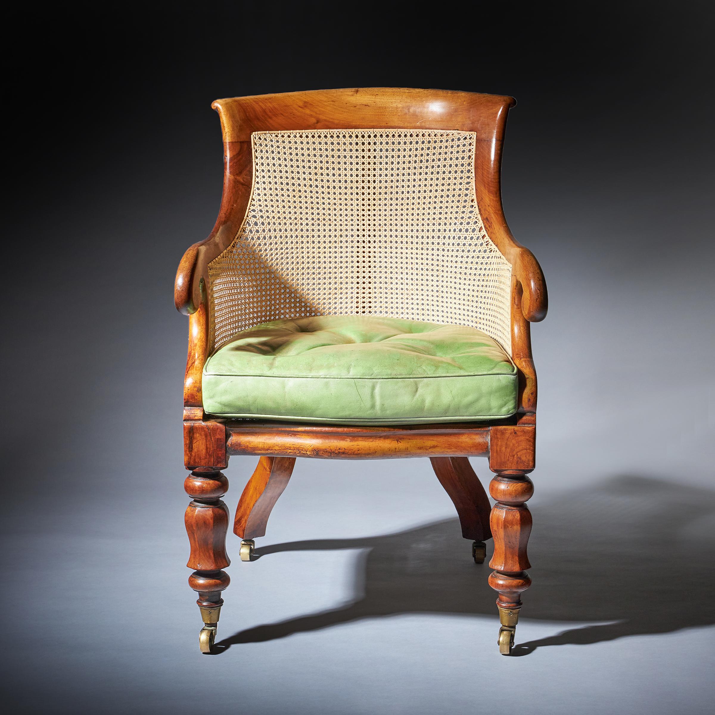 A 19th century William IV mahogany Bergere armchair with curved top rail cane panel back and sides with scroll arm supports. The cane panel seat with the original buttoned green leather loose cushion on turned and shaped legs, terminating on brass