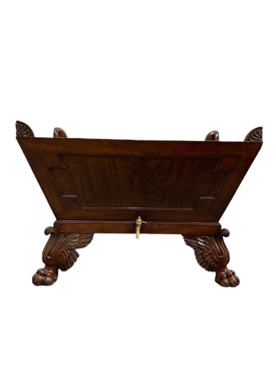 19th Century William IV Mahogany Jardiniere/Cellarette of sarcophagus form, each corner mounted with an anthemion carving, the case with figured panels, the interior with a tole liner, the base fitted with a metal drain spigot, and raised on
