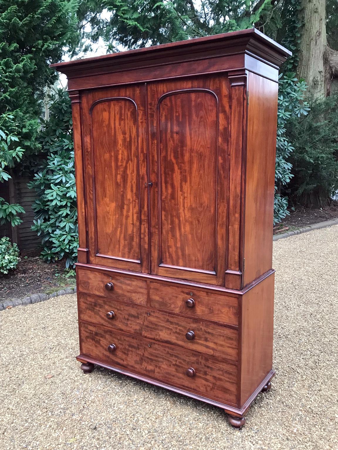 19th century William IV mahogany linen press with two panelled doors and four original interior sliding trays. Two short and two long solid oak lined drawers with original turned bun handles and turned feet. Comes apart in three separate