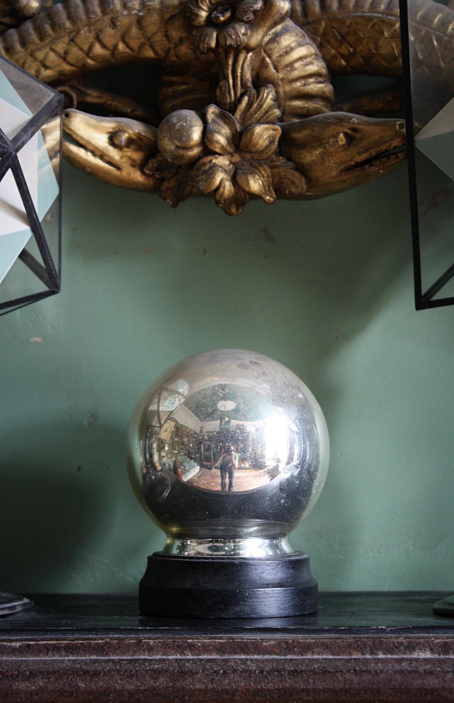 A 19th century mercury glass witches ball on a later purpose made ebonised stand. The witches ball has a small glass lipped base that sits perfectly on the stand. 

The ball is heavily foxed around the top third and this gradually wanes as you move