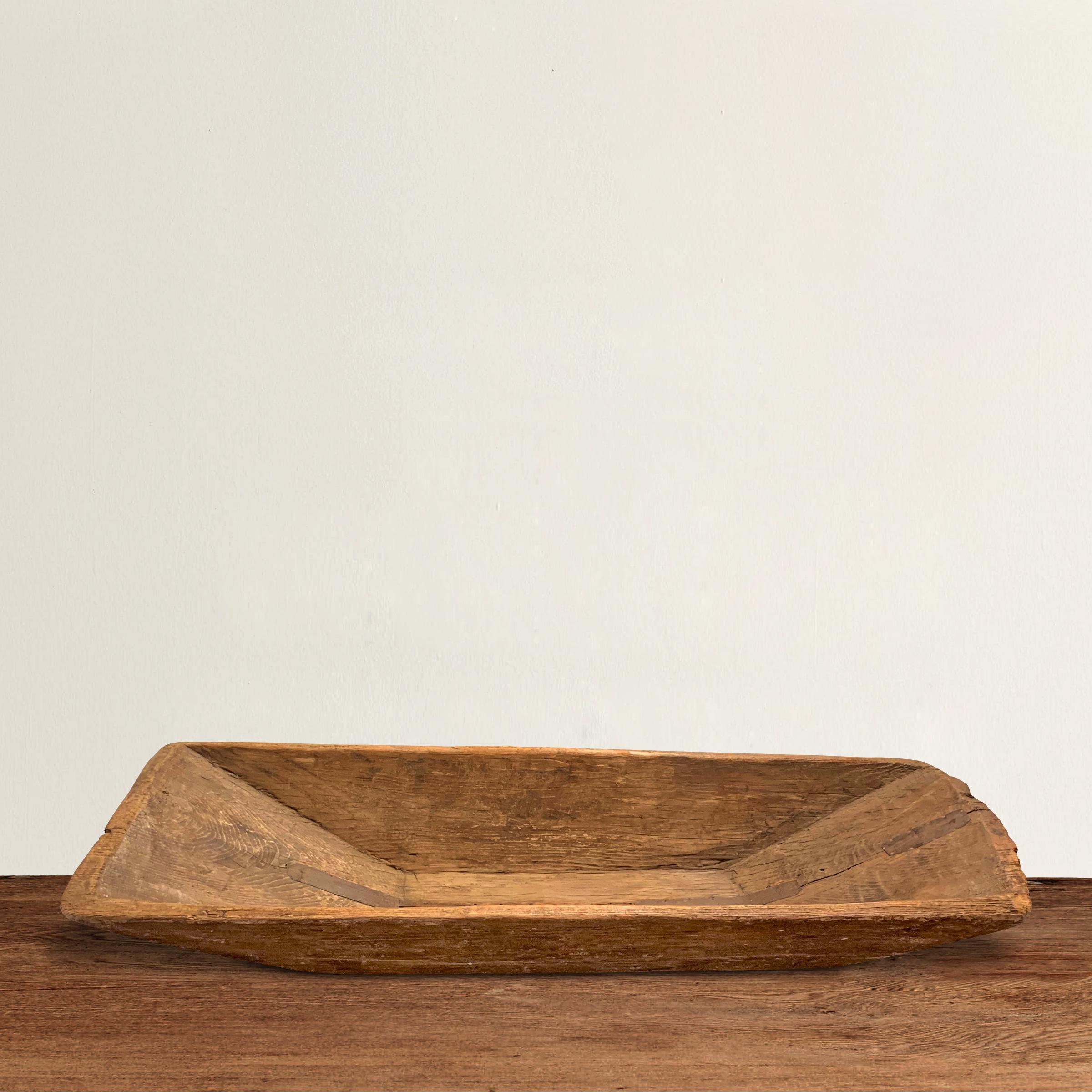 A fantastic and large 19th century American hand carved wood dough trough of rectangular form with tapered sides and a handle carved of the same piece of wood, retaining original old metal repairs.