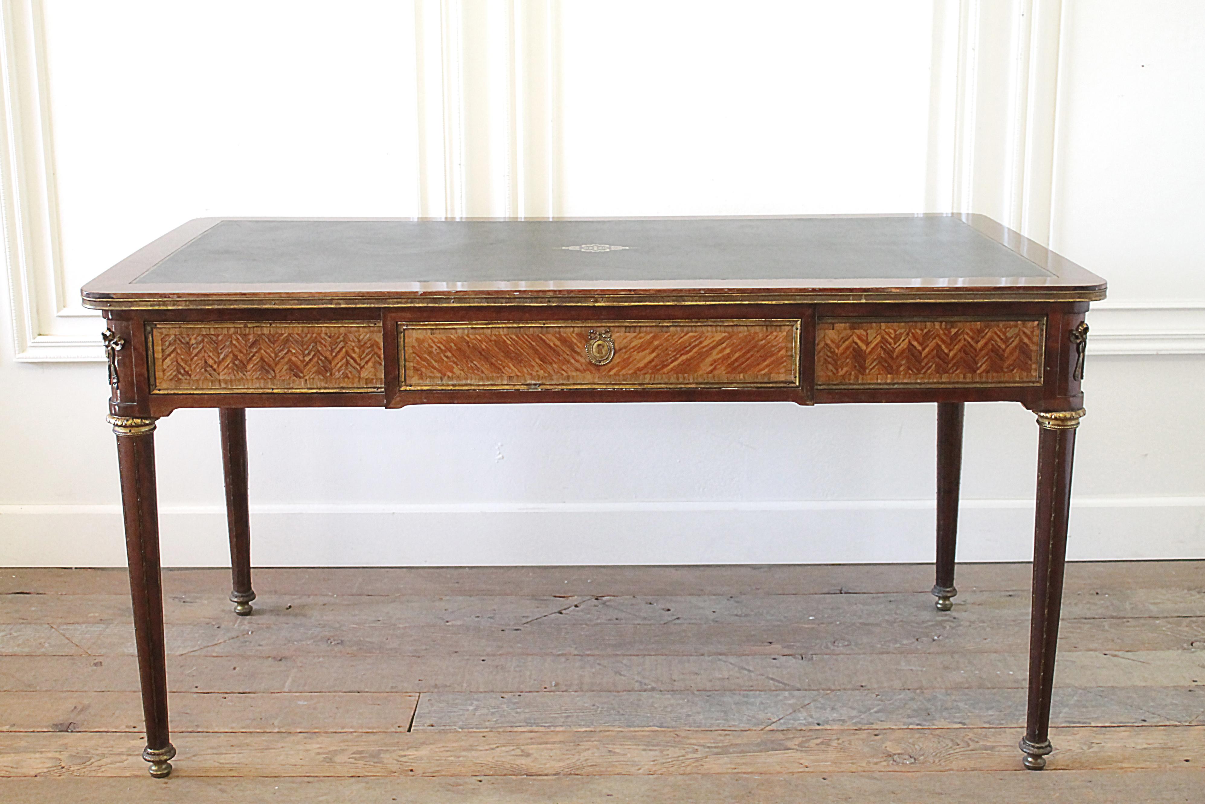 19th century wood inlay Louis XVI style leather top desk
This desk has beautiful chevron style wood inlays, and bronze mounted ormolu ribbons on the corners. Decorative bronze caps at the top of the legs, and feet, as well as down the flutes of