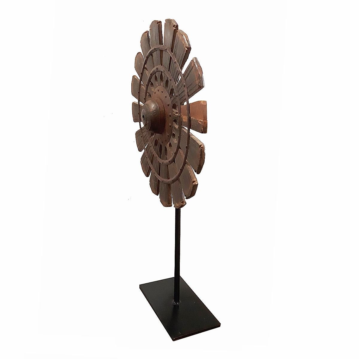 Once a part of an antique  loom, this spinning wheel was hand carved out of a single piece of teak wood, with iron center and rivets. Mounted on a black metal stand.