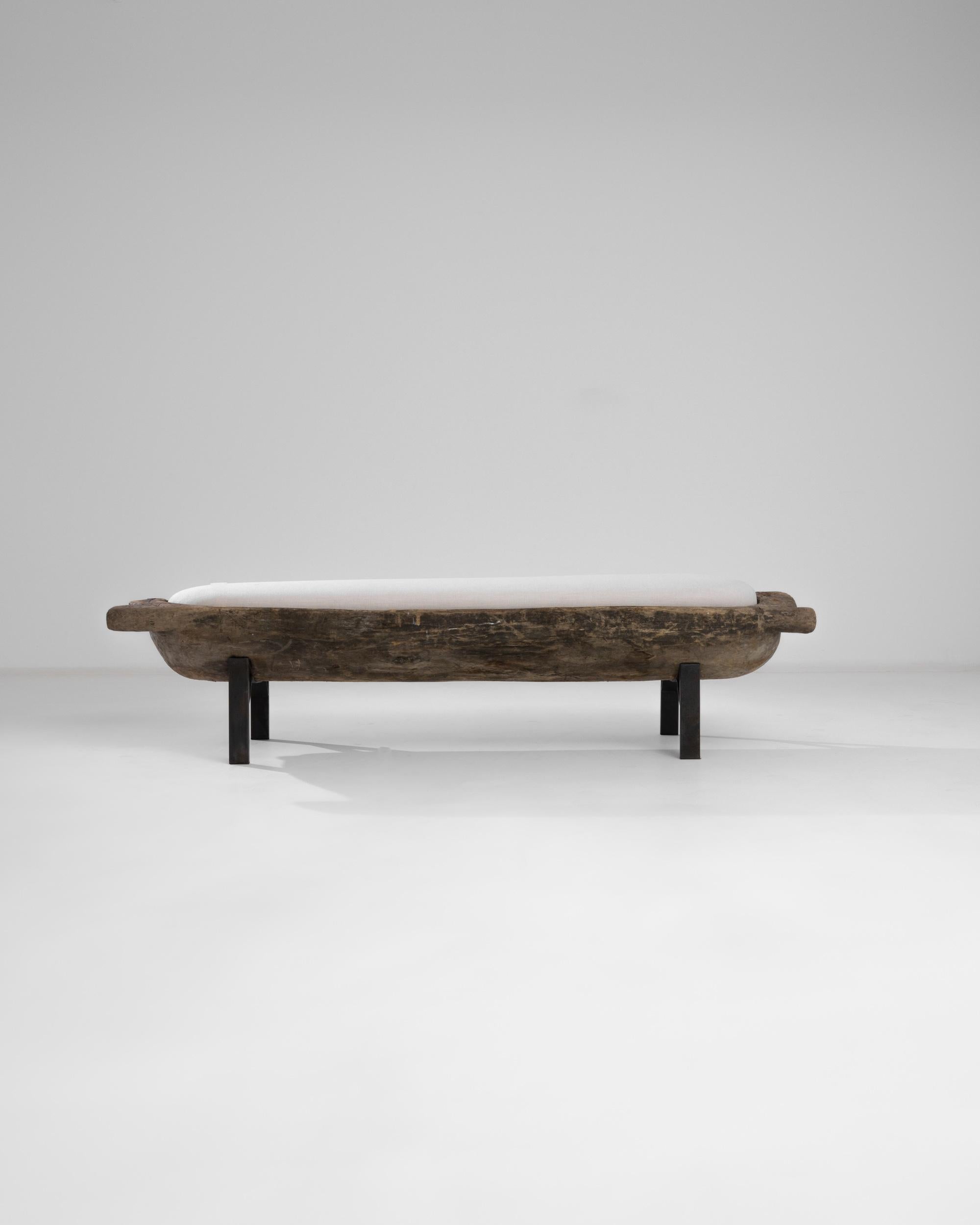 A 19th century wooden bench with an upholstered seat from Poland. A carved wooden bread trough resembling a pagoda is elevated upon black metal feet, completed by a comfortable upholstered ecru seat. The smoked coffee tone of the century-old patina