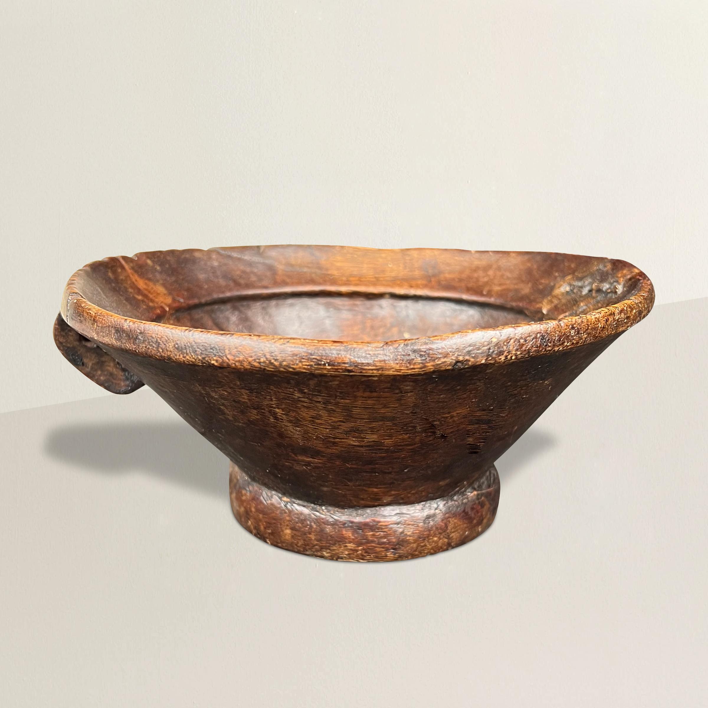 Embrace the rustic charm and storied history of this hand-carved primitive wood bowl. Crafted with care by skilled artisans of the past, its weathered appearance bears witness to a life well-lived. The most intriguing feature is the sturdy metal