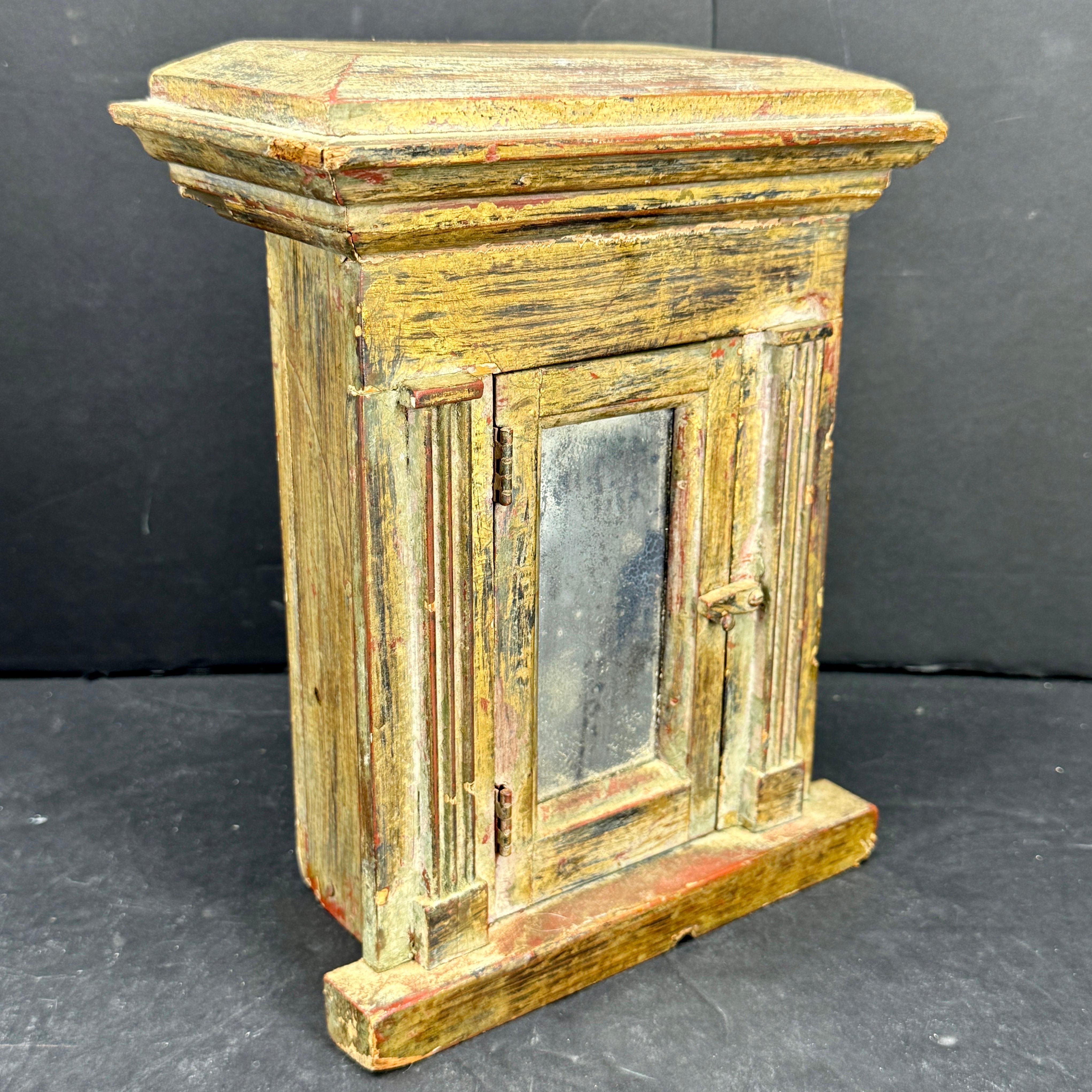 Vitrina europea del siglo XIX, de madera tallada y pintada, con puerta de cierre de cristal de espejo. Esta pieza versátil podría utilizarse para guardar joyas o coleccionables. También vemos que este mueble podría haber sido una pieza religiosa y