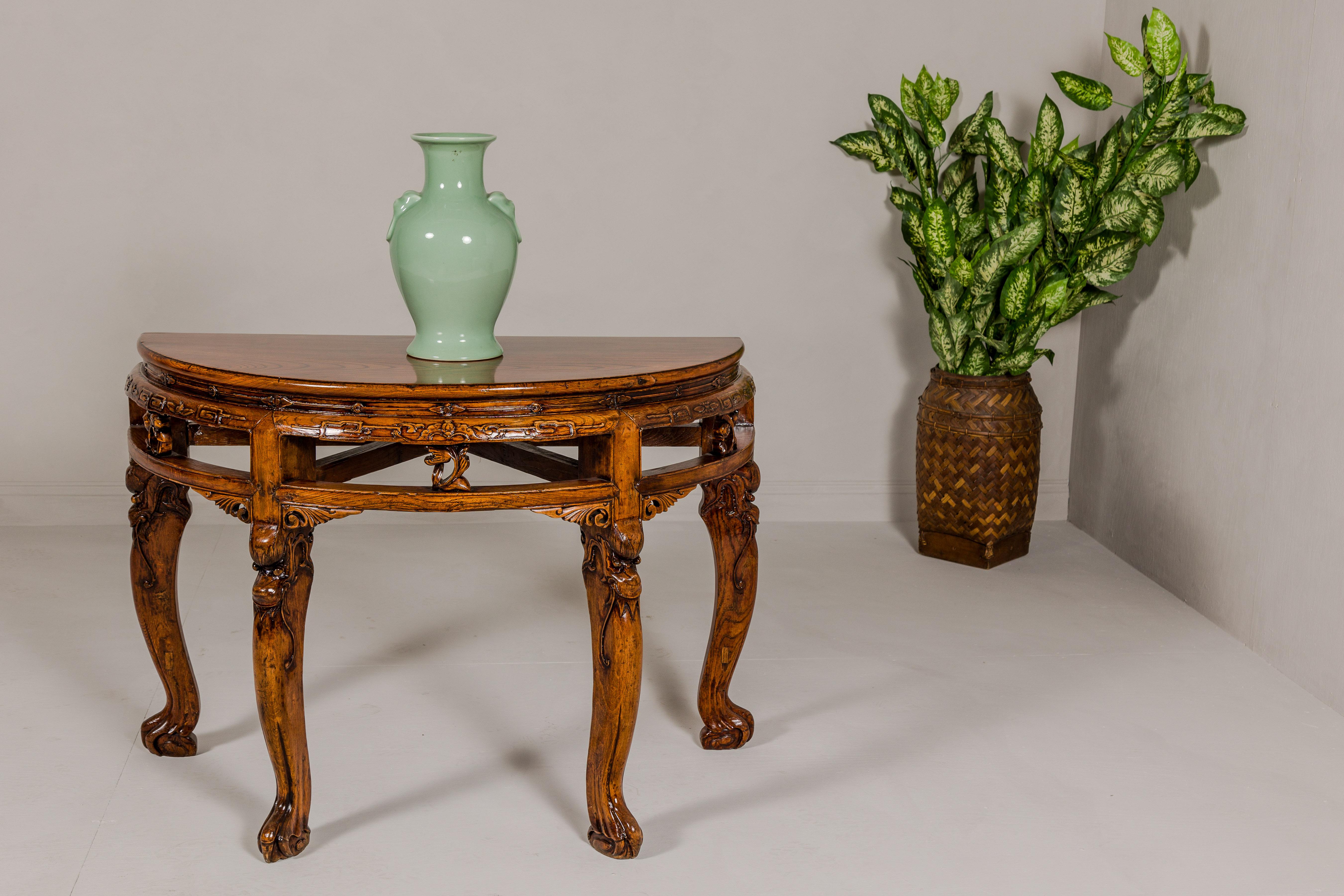 A Qing Dynasty period wooden demilune table from the 19th century with carved apron and mythical creatures on the legs. This Qing Dynasty period wooden demilune table, hailing from the 19th century, is a magnificent testament to the rich cultural