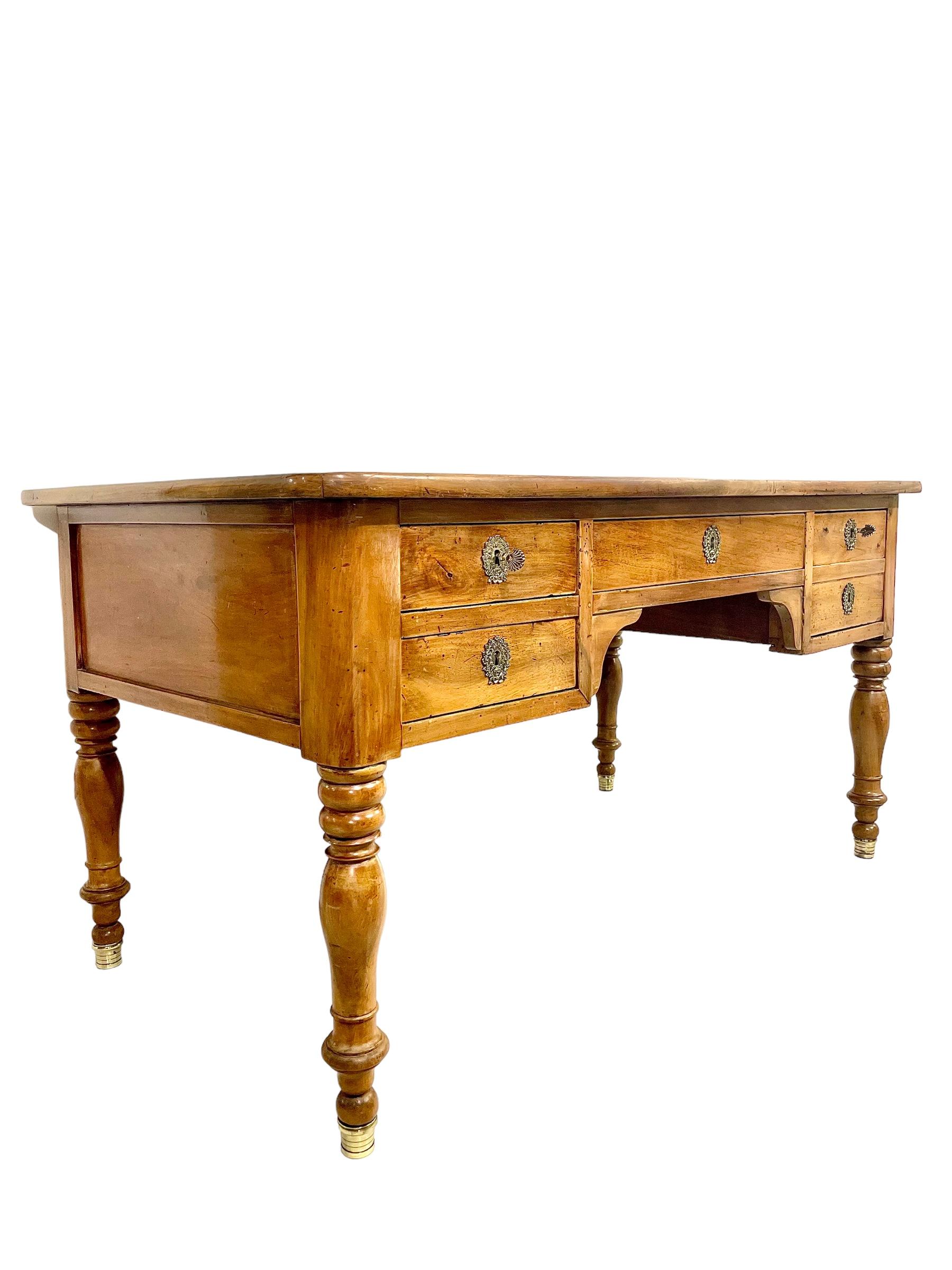 A very handsome 19th century partners' desk with five drawers. The finish is natural wood, with smoothly rounded corners and sturdy turned legs terminating in brass sabots. The rectangular top is inlaid with gold tooled green leather to form a