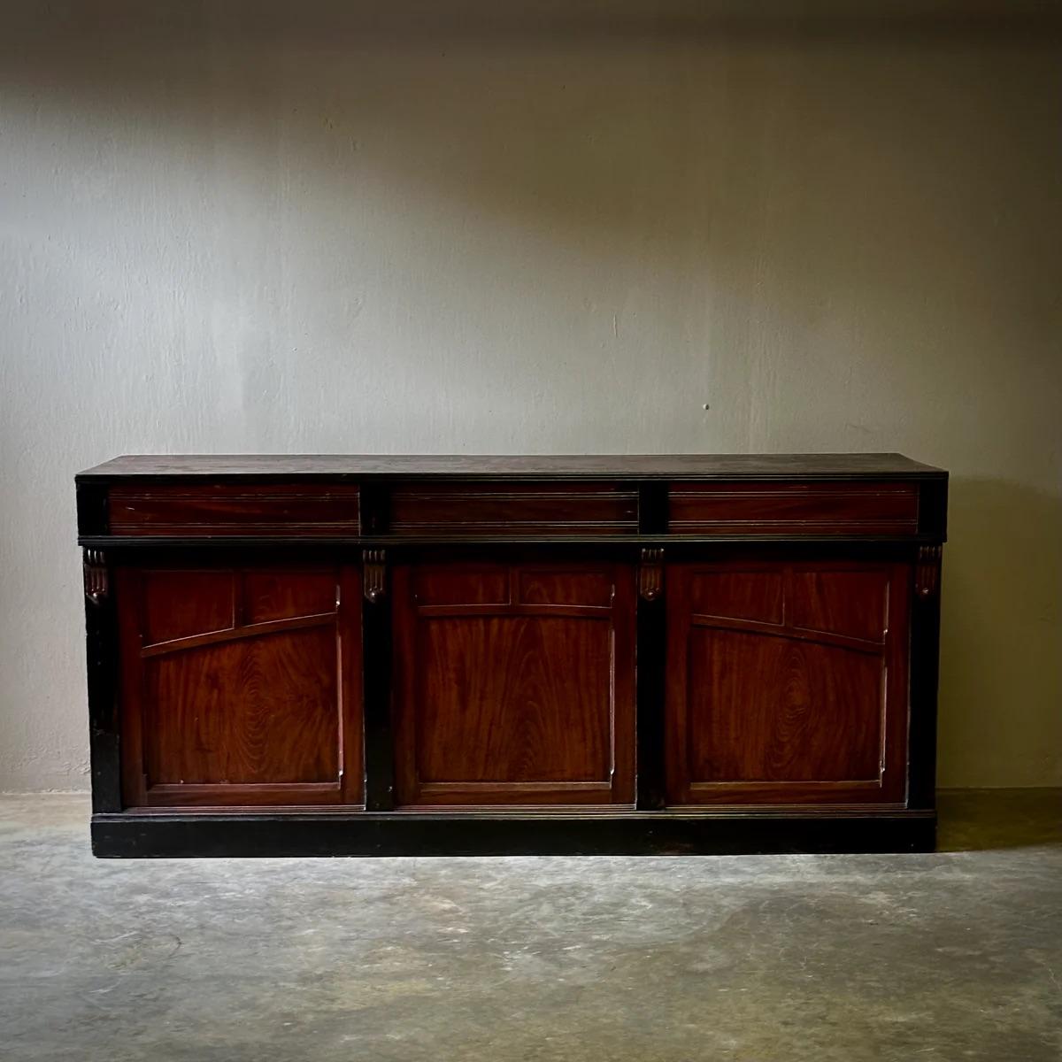 Bancone da negozio belga tradizionale del XIX secolo con finitura originale verniciata in tonalità scura. Adatto come credenza o credenza, questo pezzo robusto offre una miscela accattivante di design utilitario e fascino estetico, grazie a una