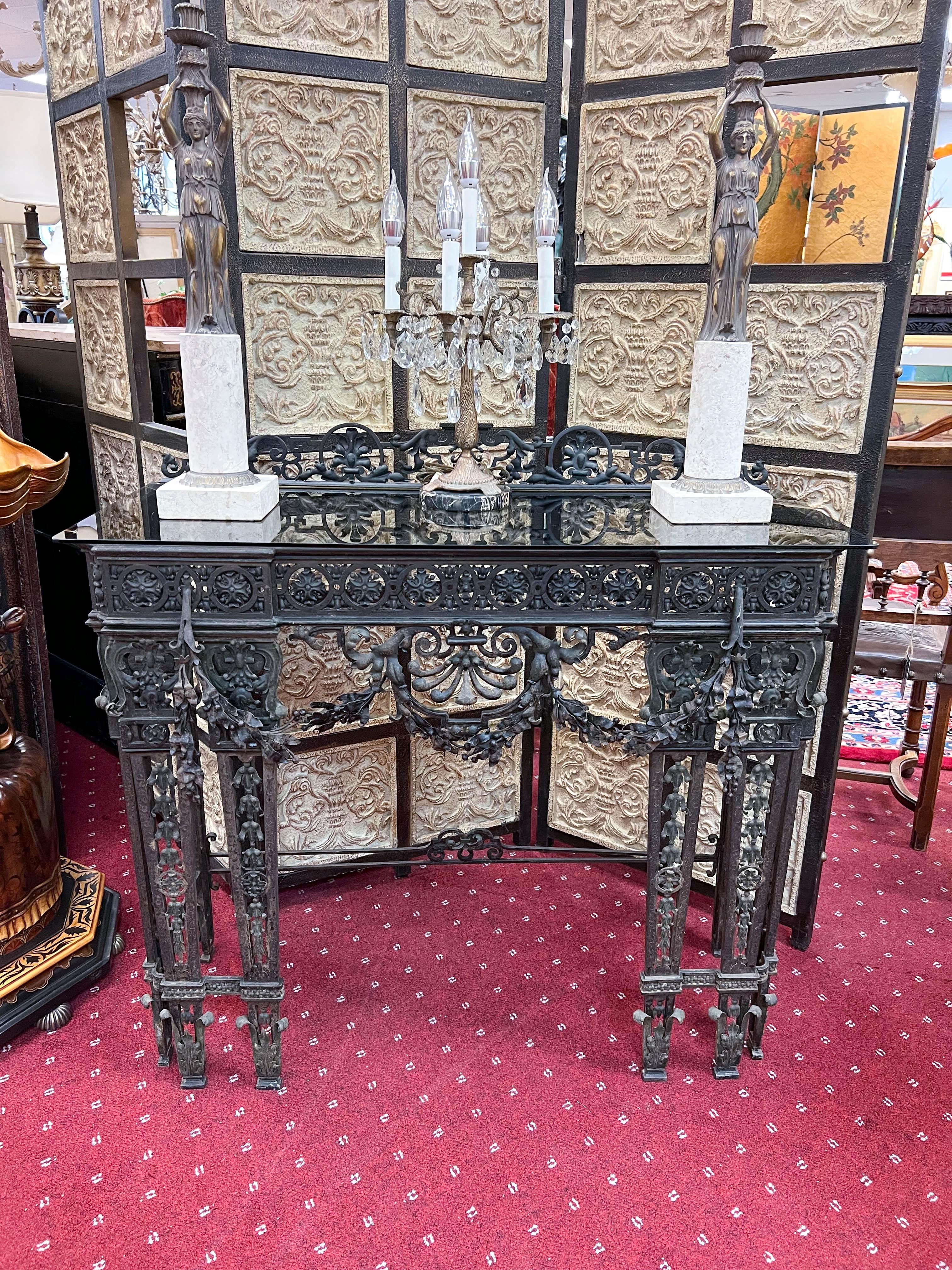 Handcrafted circa 1875 by a metal artist schooled in Europe, the antique wrought iron console table is topped with a 1/4 inch smoky glass.  The delicate metal scroll details throughout and garland along the front apron make this a one-of-a-kind