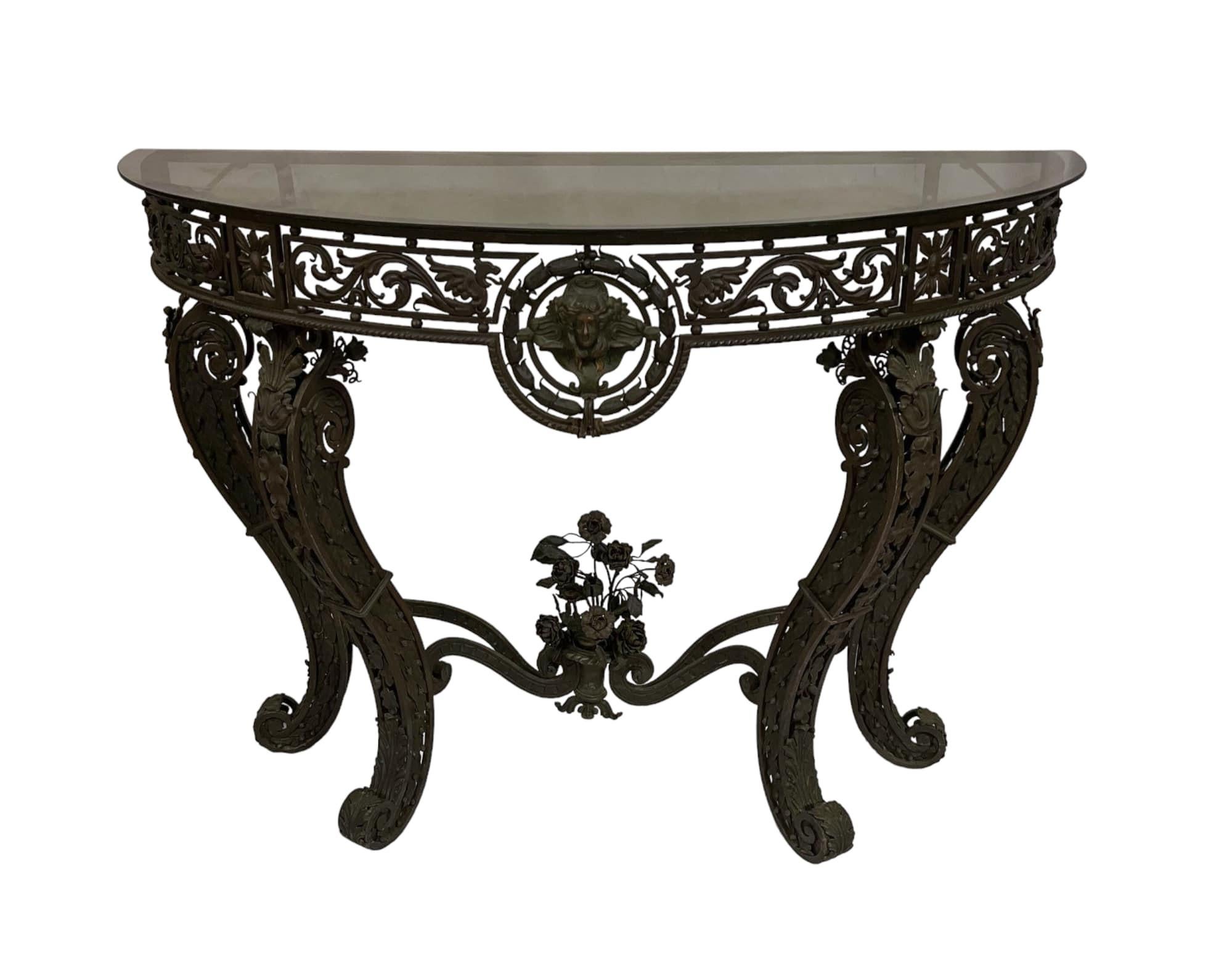 Handcrafted circa 1875 by a metal artist schooled in Europe, the antique wrought iron demi-lune console table is topped with a 1/4 inch smoky glass. It stands on cabriole-shaped legs adorned with the most intricate metal floral embellishments.